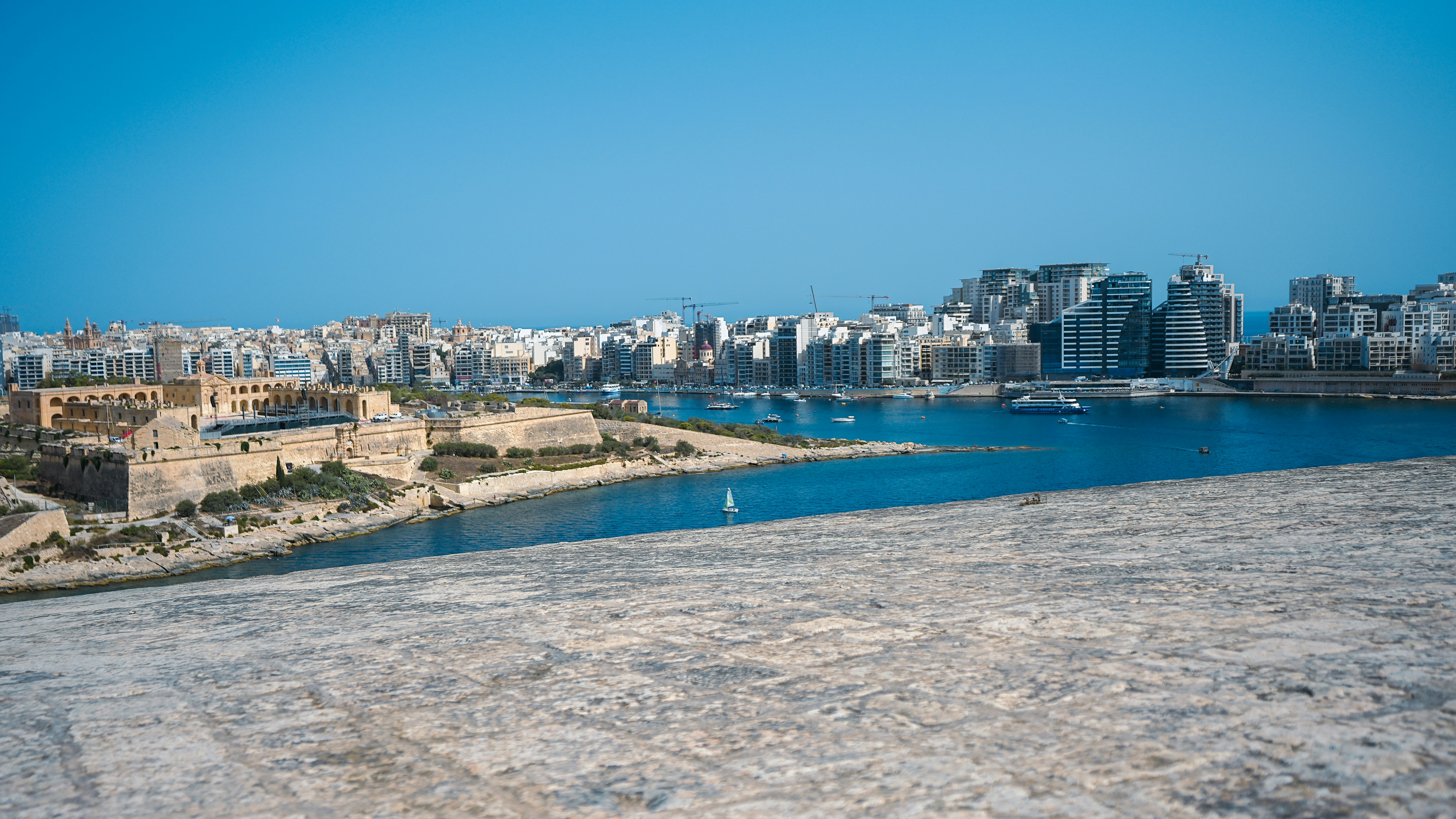 A stone fortification overlooking a bay with a modern city skyline in Valletta, Malta