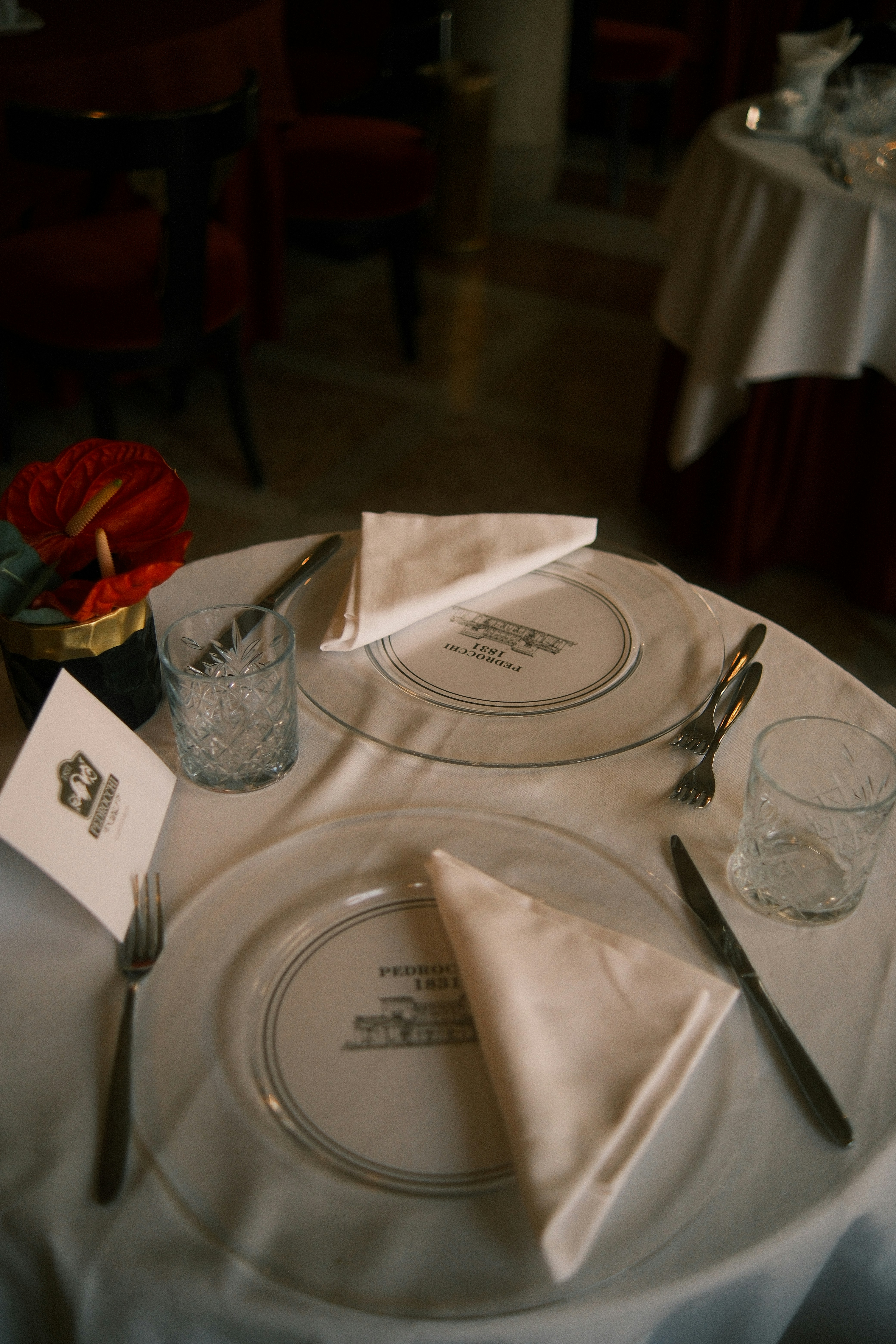 A table set for two with white napkins, glass plates, and crystal tumblers