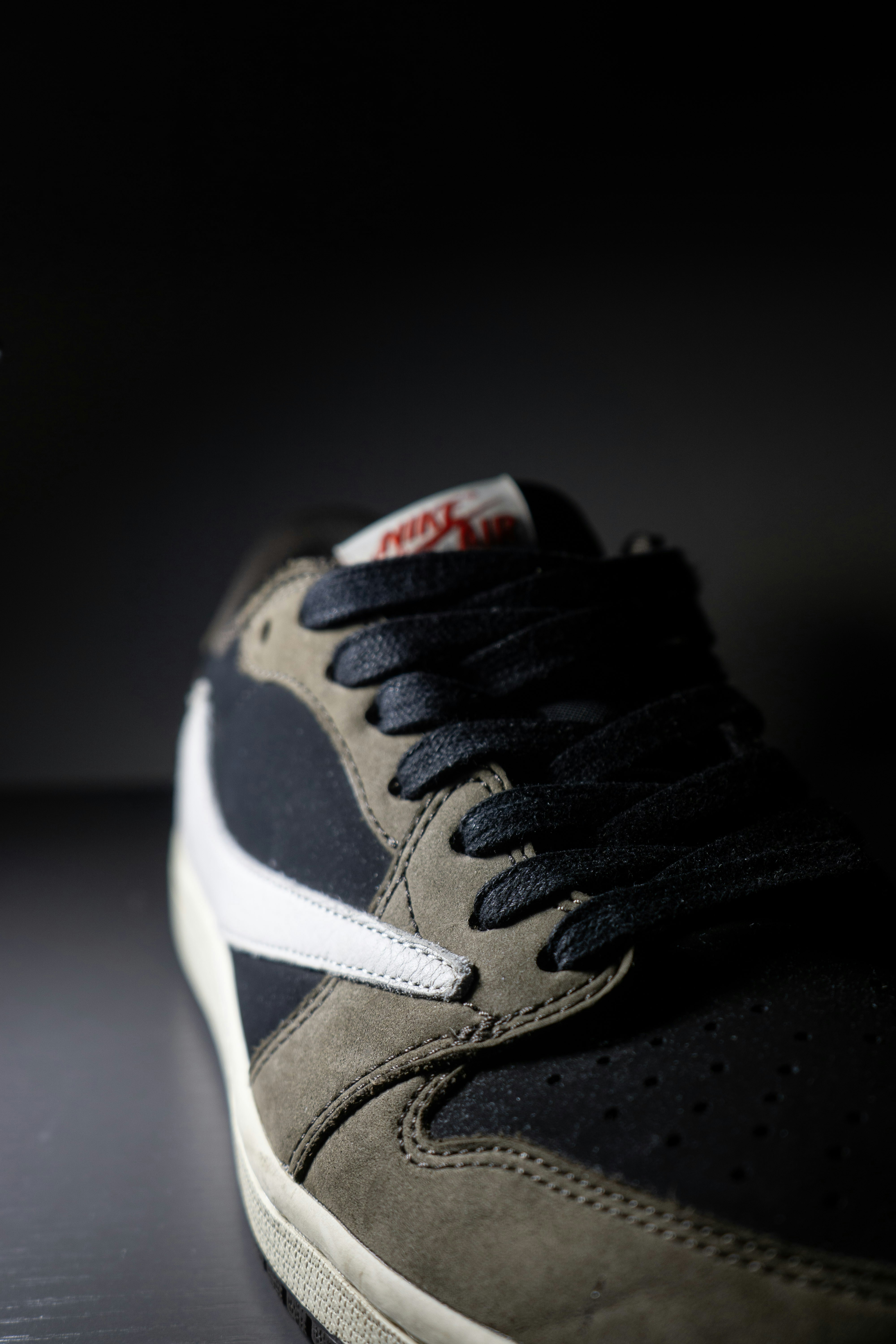 A black and olive suede sneaker with a white swoosh on a dark surface