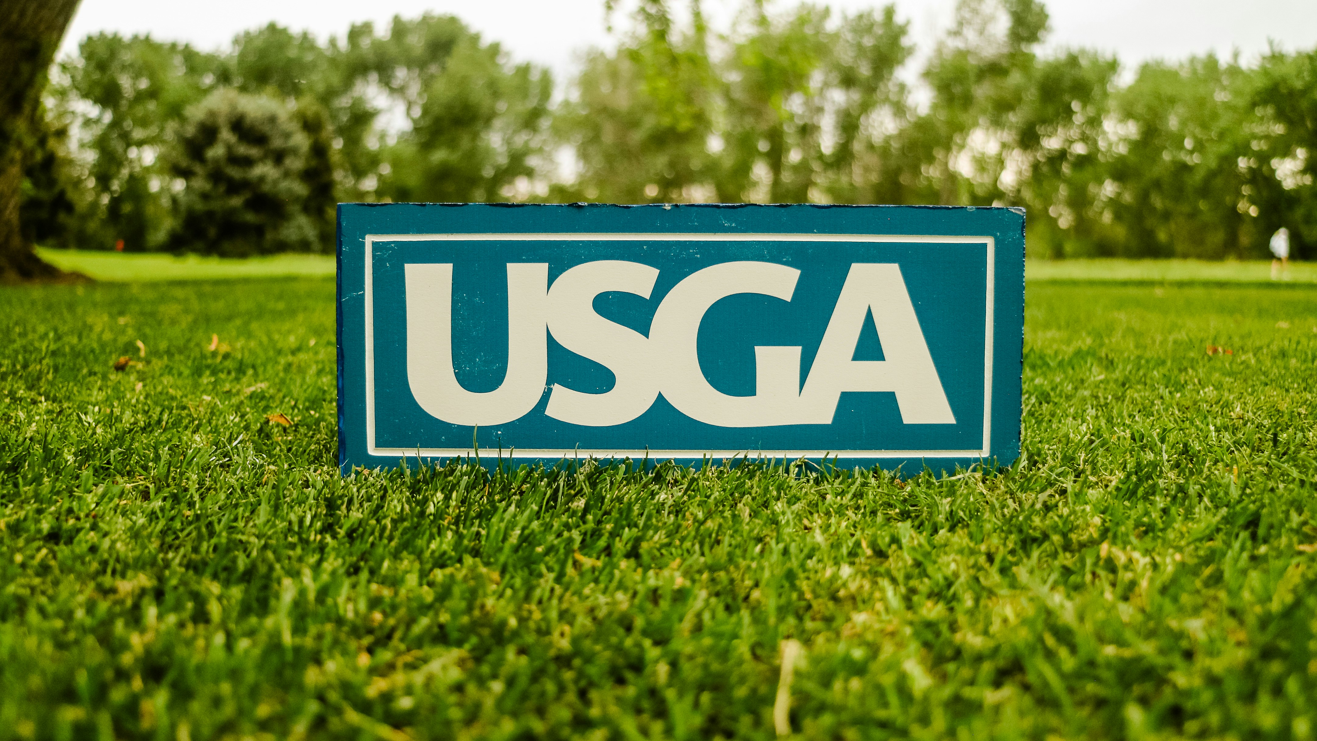 A blue sign with white USGA lettering on a green golf course lawn