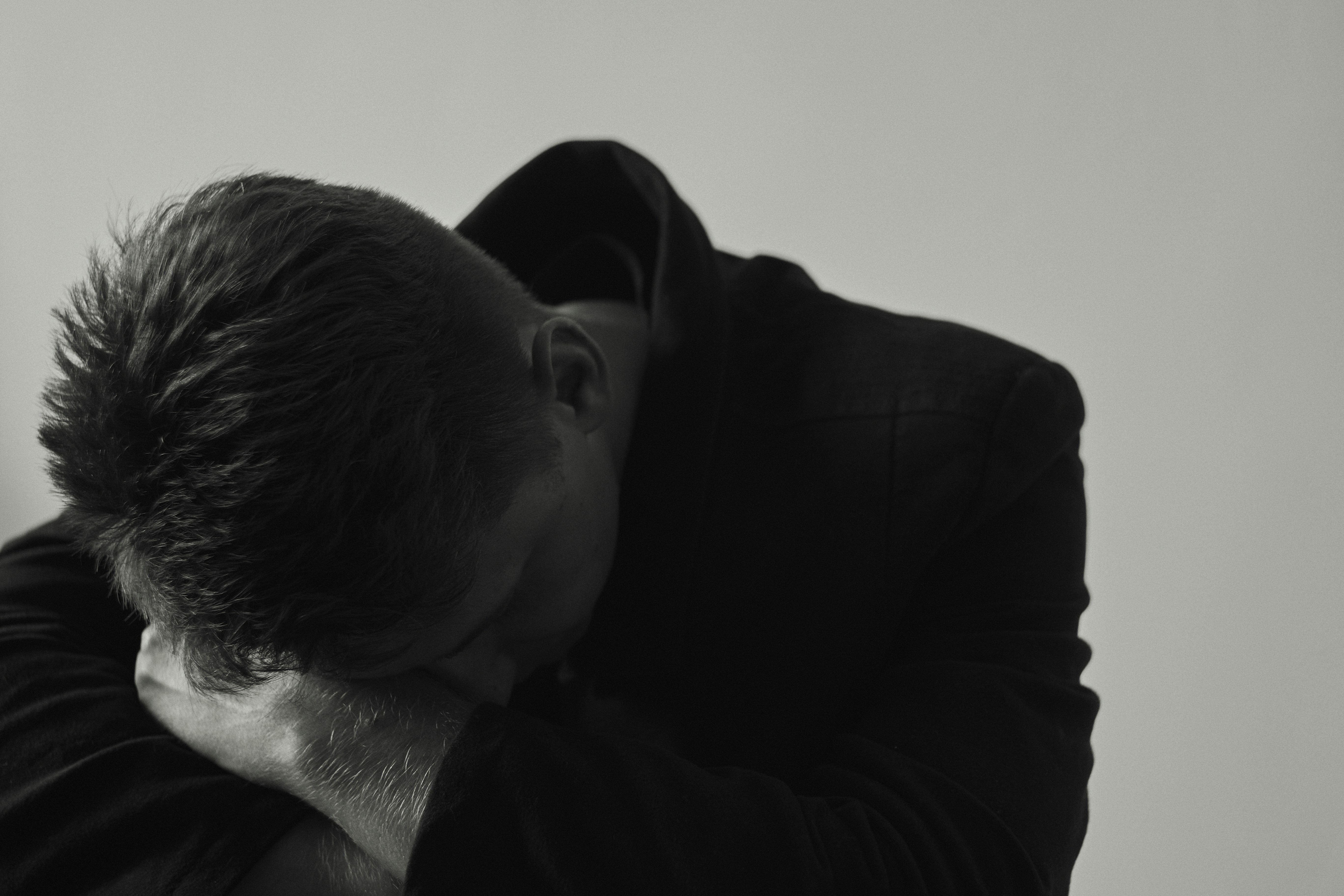 A person in a black jacket with their head resting on their arms