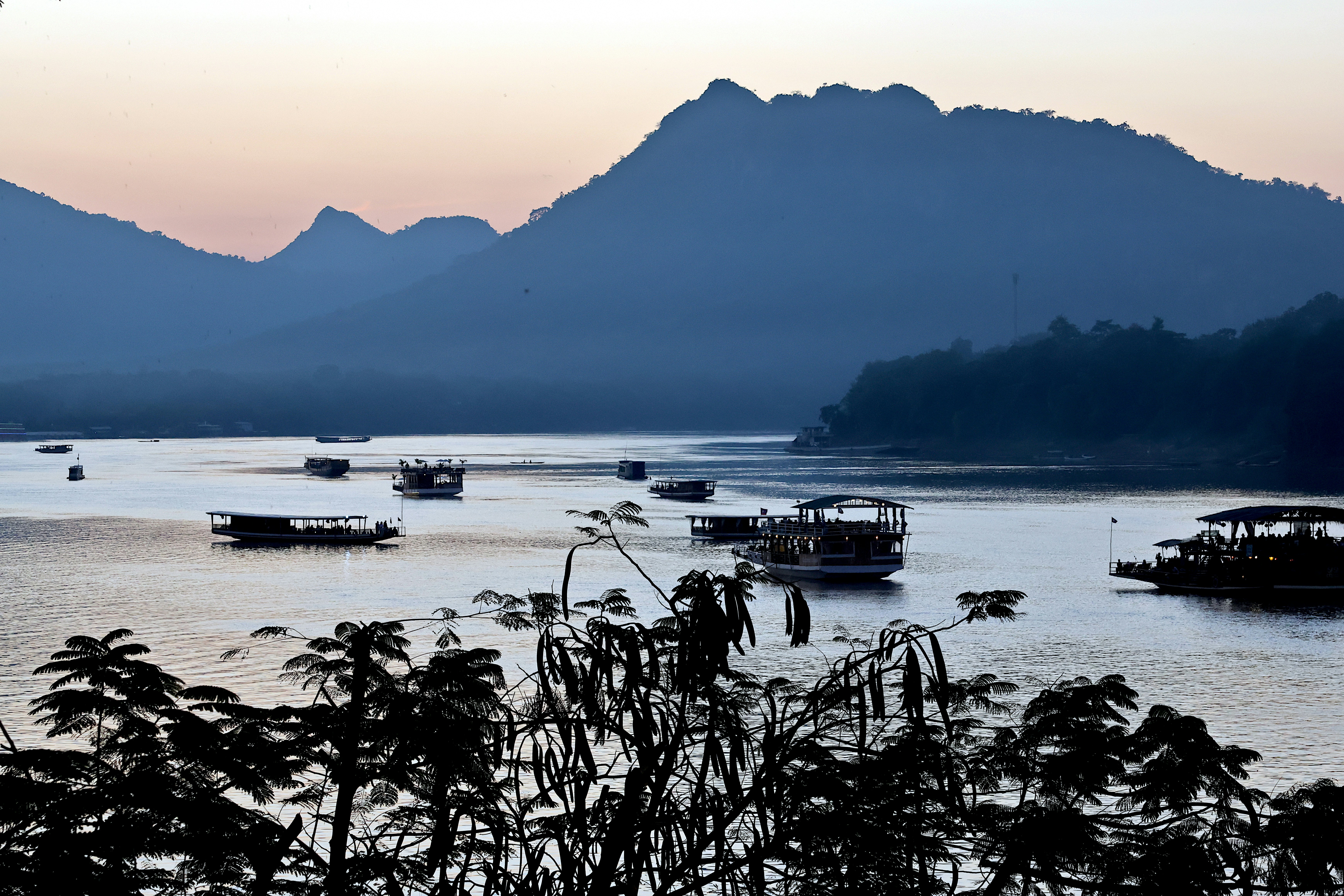 The Mekong at dusk in Luang Prabang, boats moored below the mountains