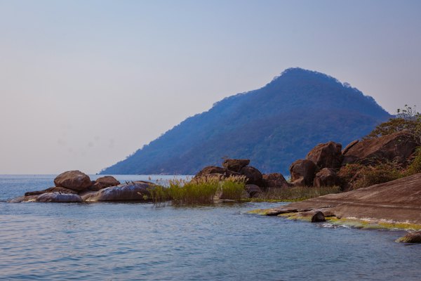 Boulders on the shore below a peak — A small motorboat moored under a leafy tree on Lake Malawi