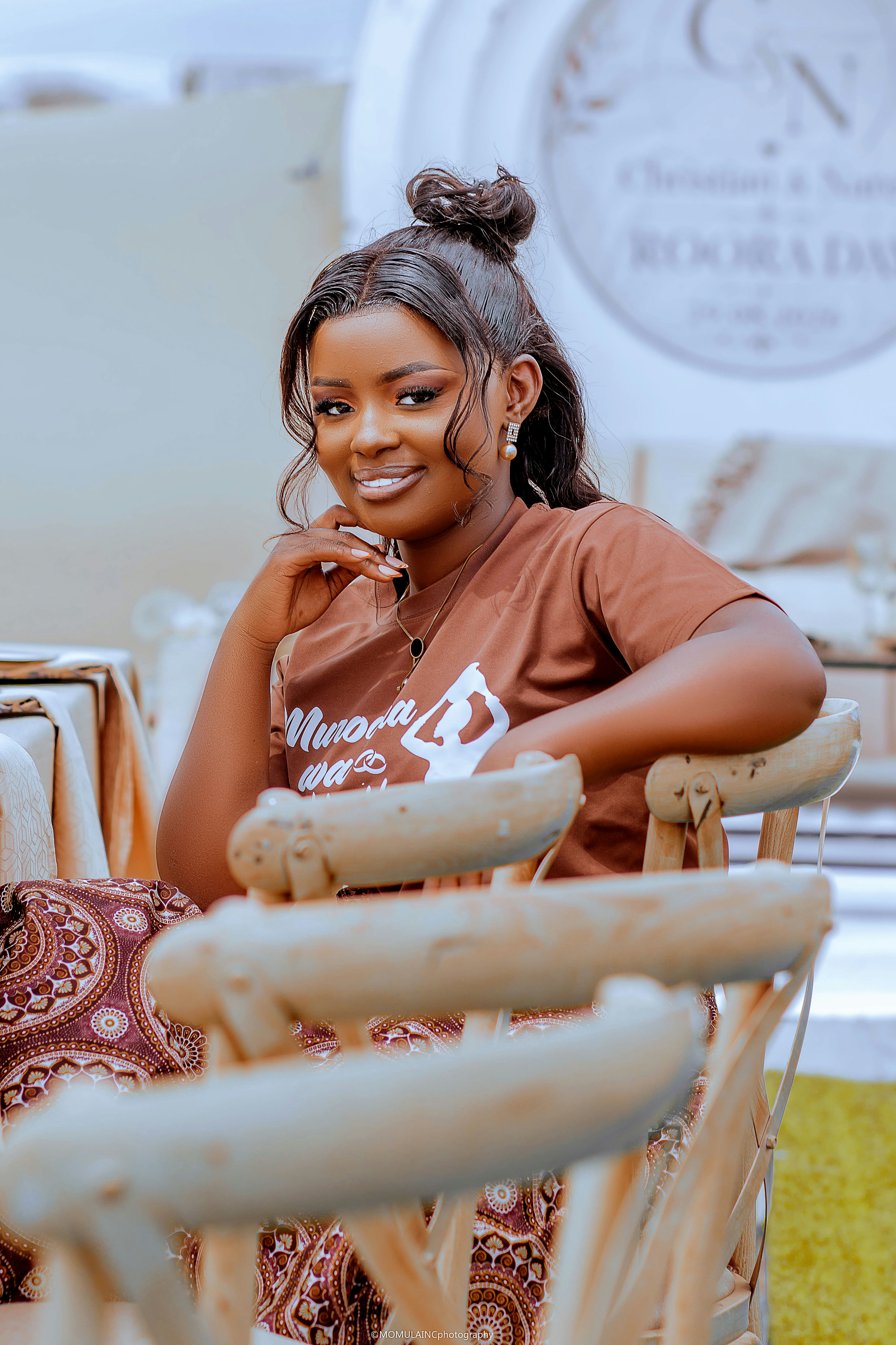 A woman with hair in a bun wearing a brown t-shirt sitting on a chair