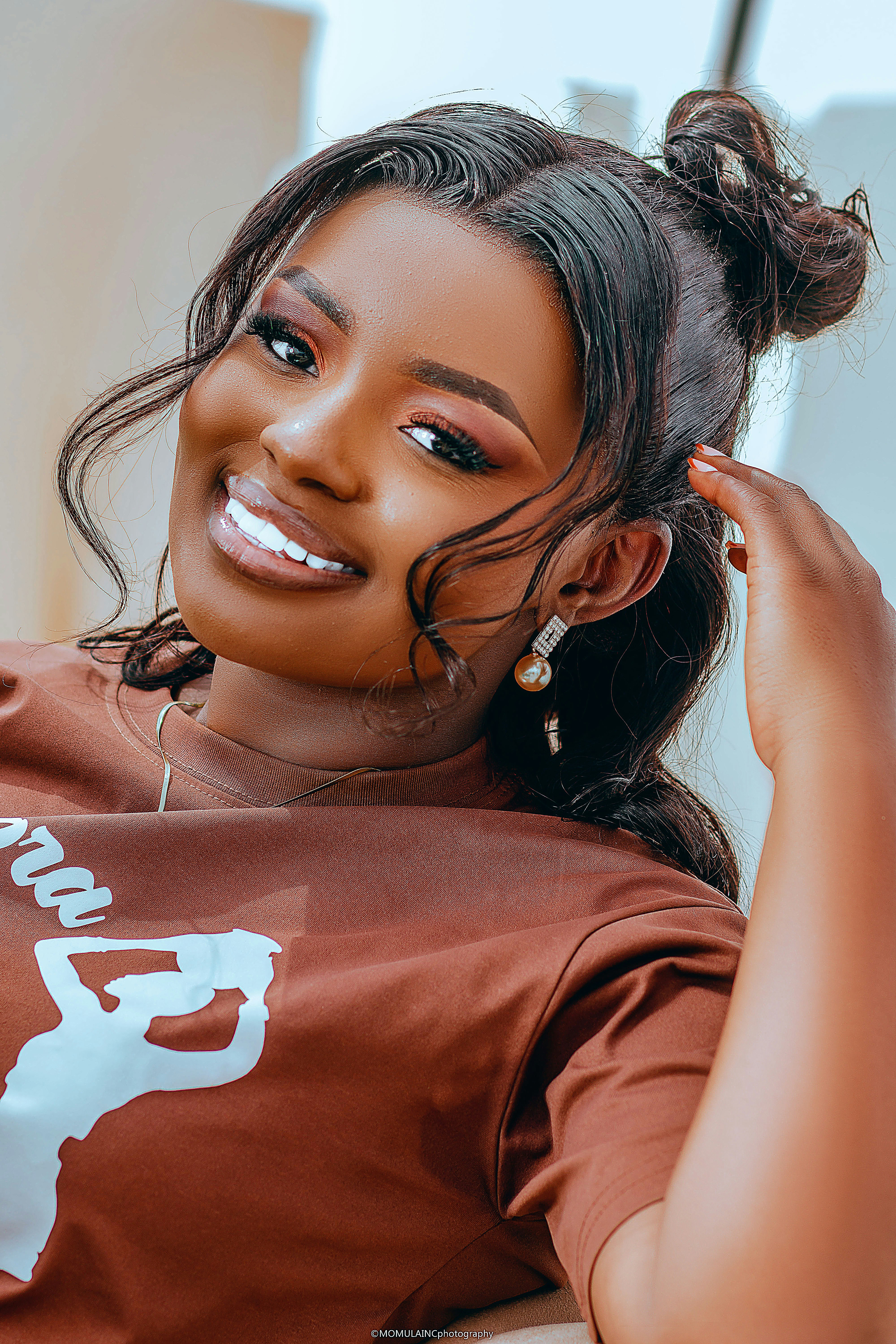 A smiling woman with dark hair in a bun wearing a brown t-shirt