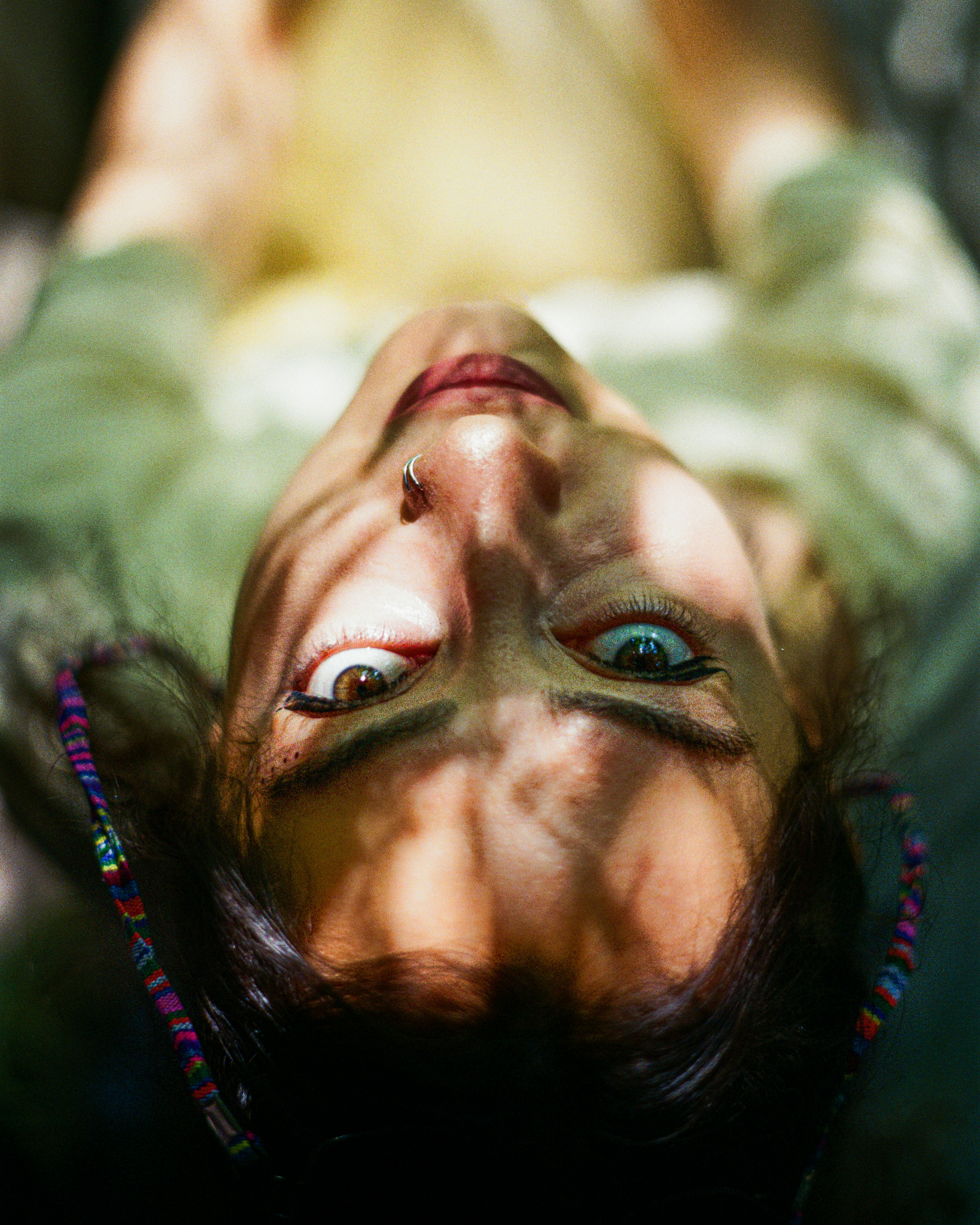 A person with a nose ring looking upward through dappled sunlight