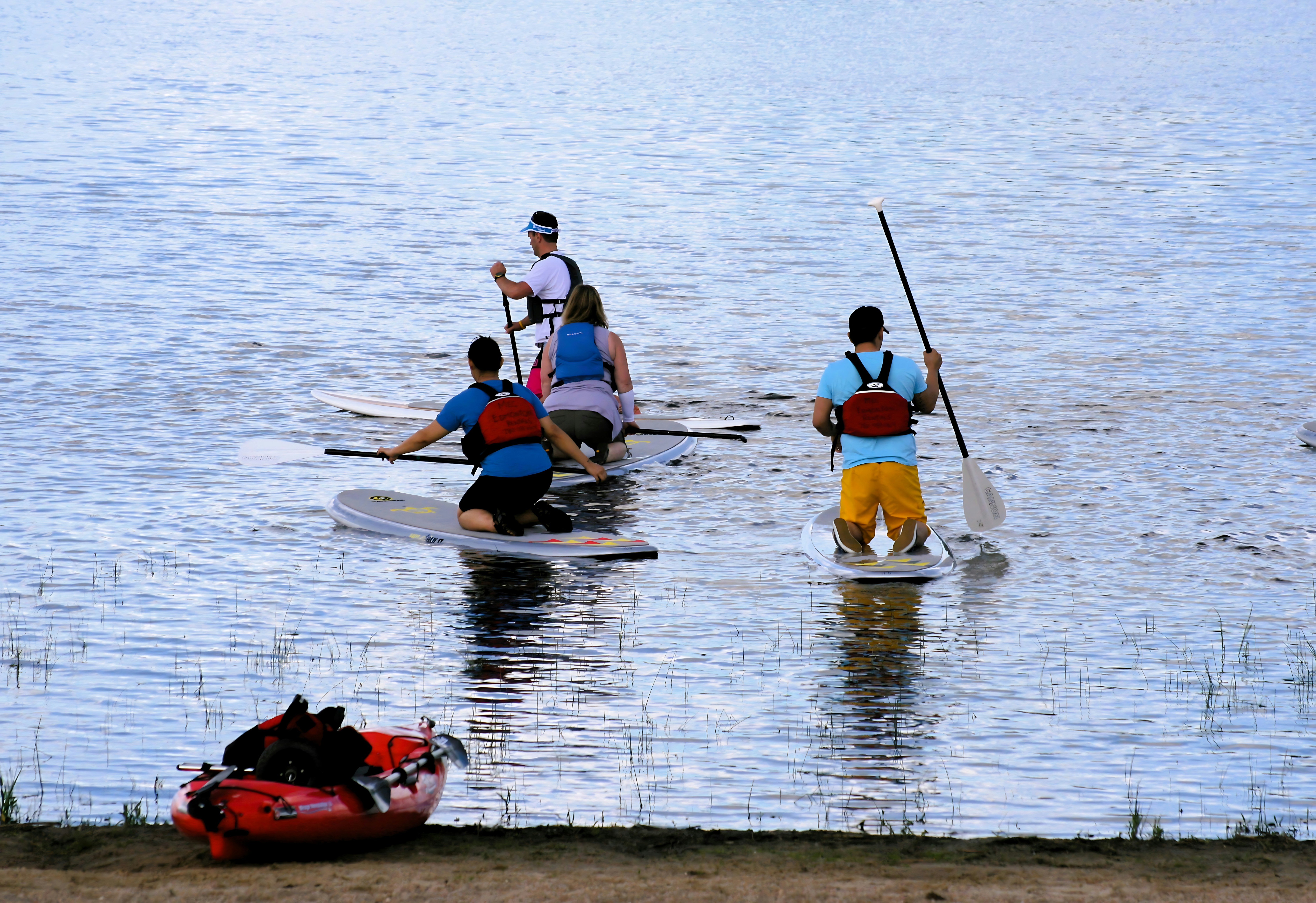 Three people on paddleboards in a lake with a red kayak nearby