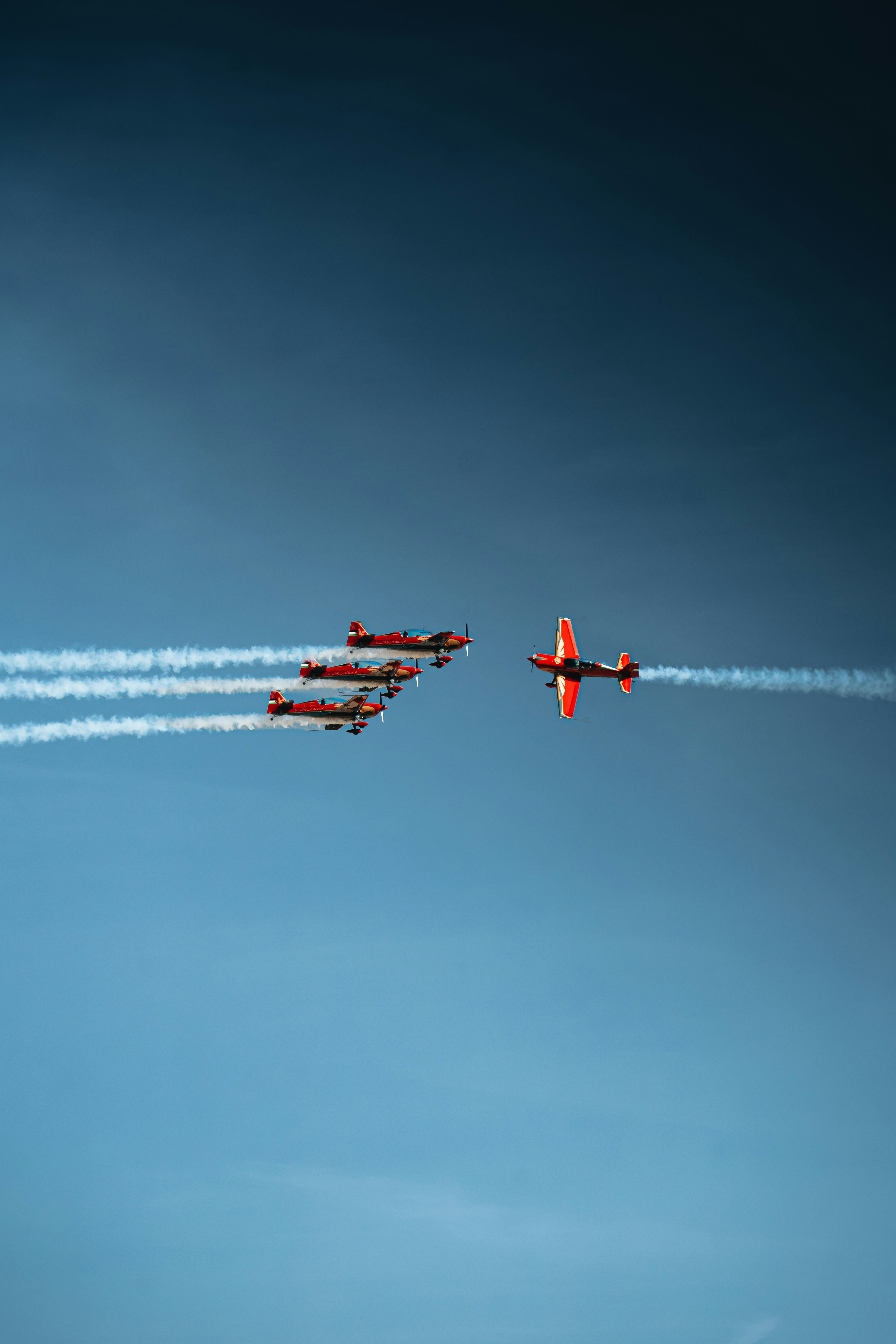 Vier rote Stuntflugzeuge fliegen in Formation gegen einen klarblauen Himmel