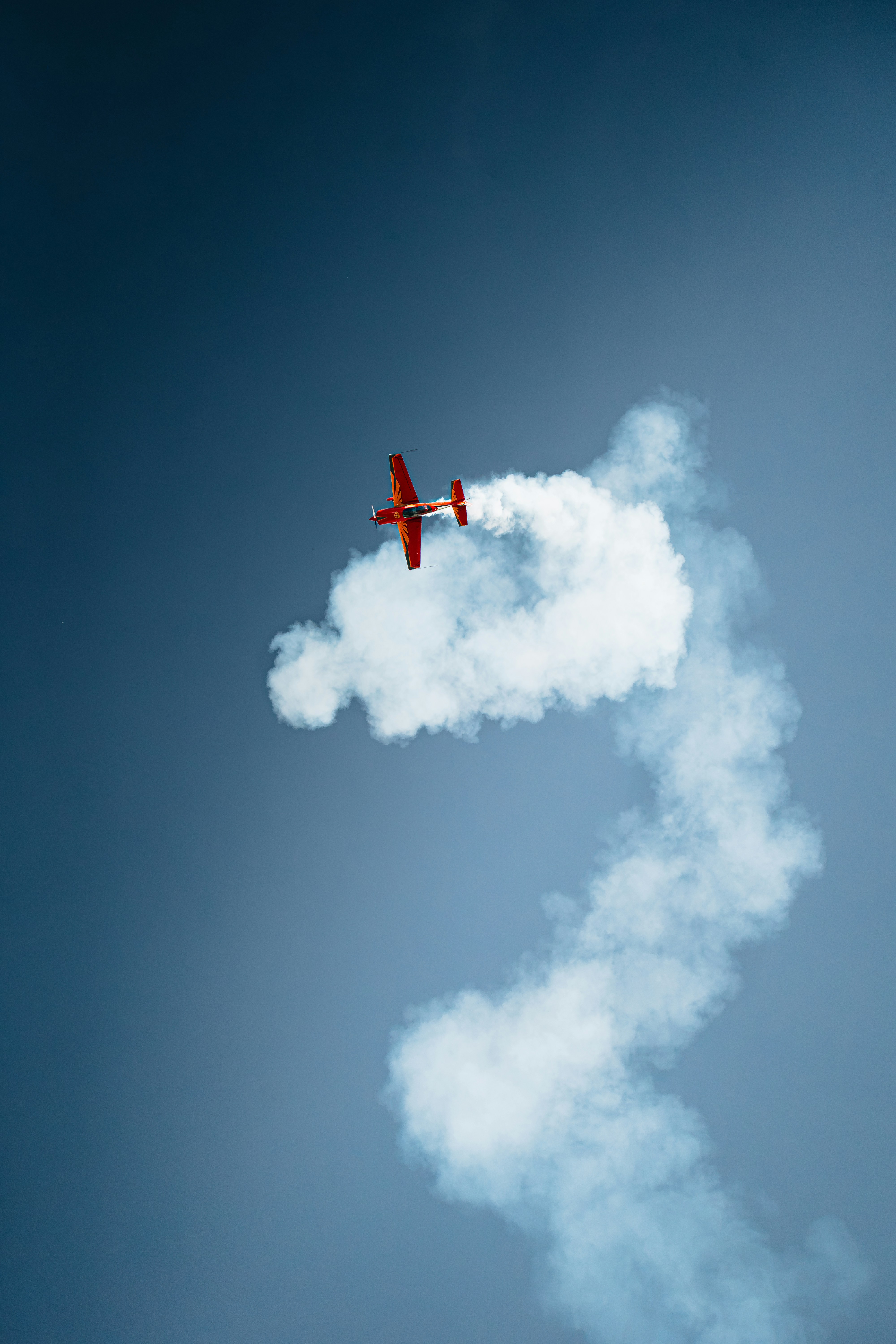A red stunt plane leaving a thick white smoke trail against a blue sky - 相关推荐