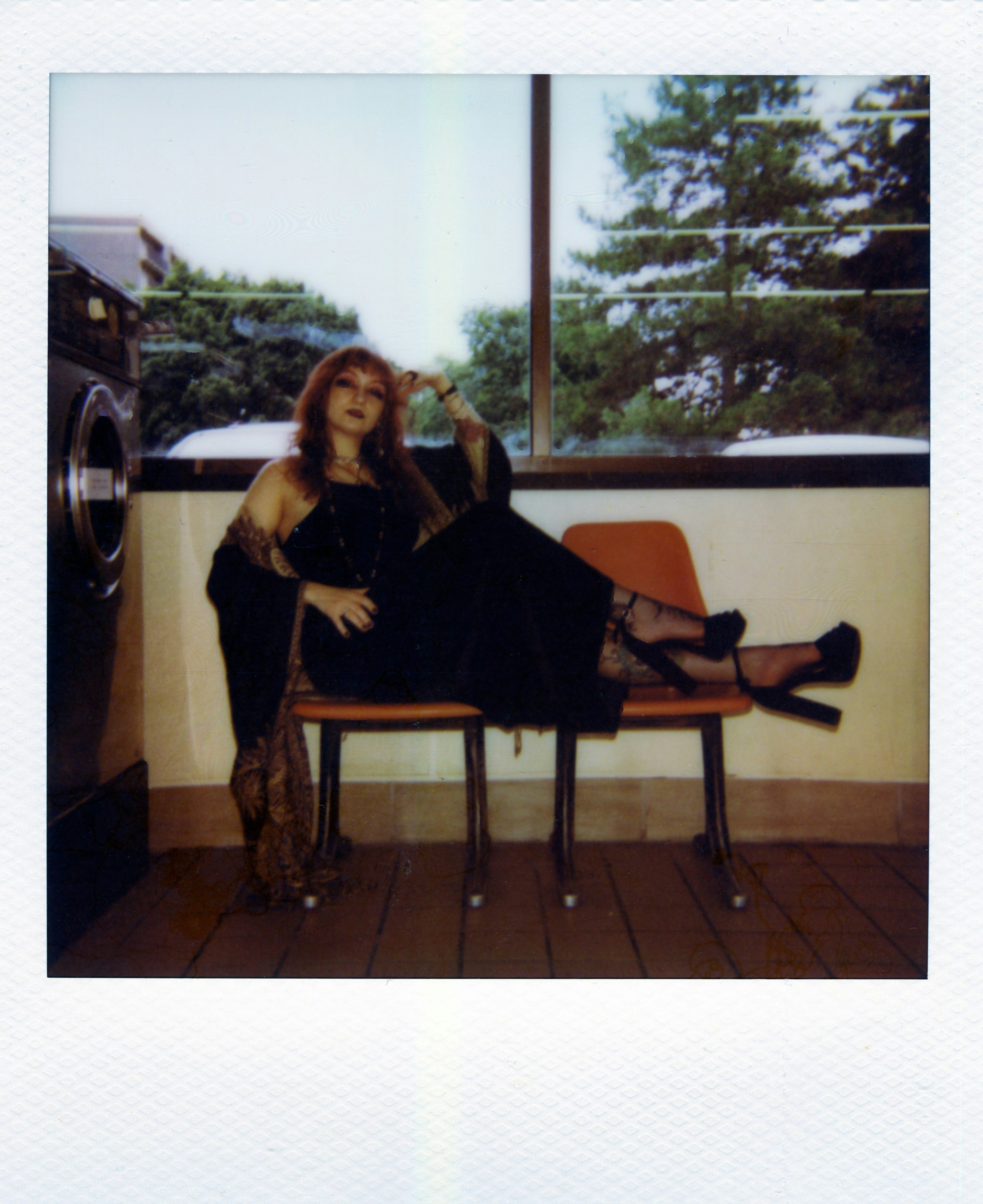 A woman in a black dress and shawl reclining on orange chairs in a laundromat