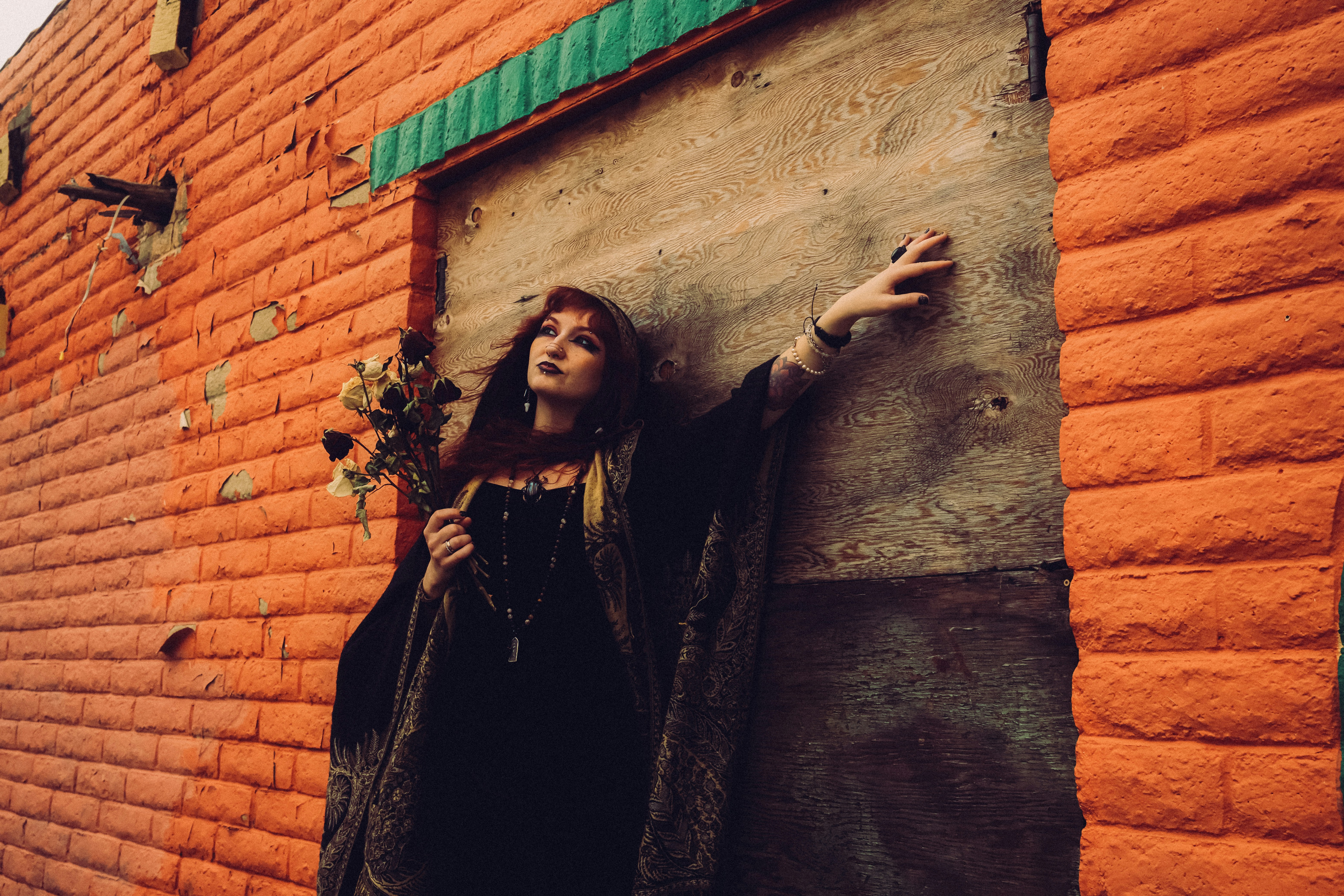 A woman in a black dress holding dried roses against an orange brick wall