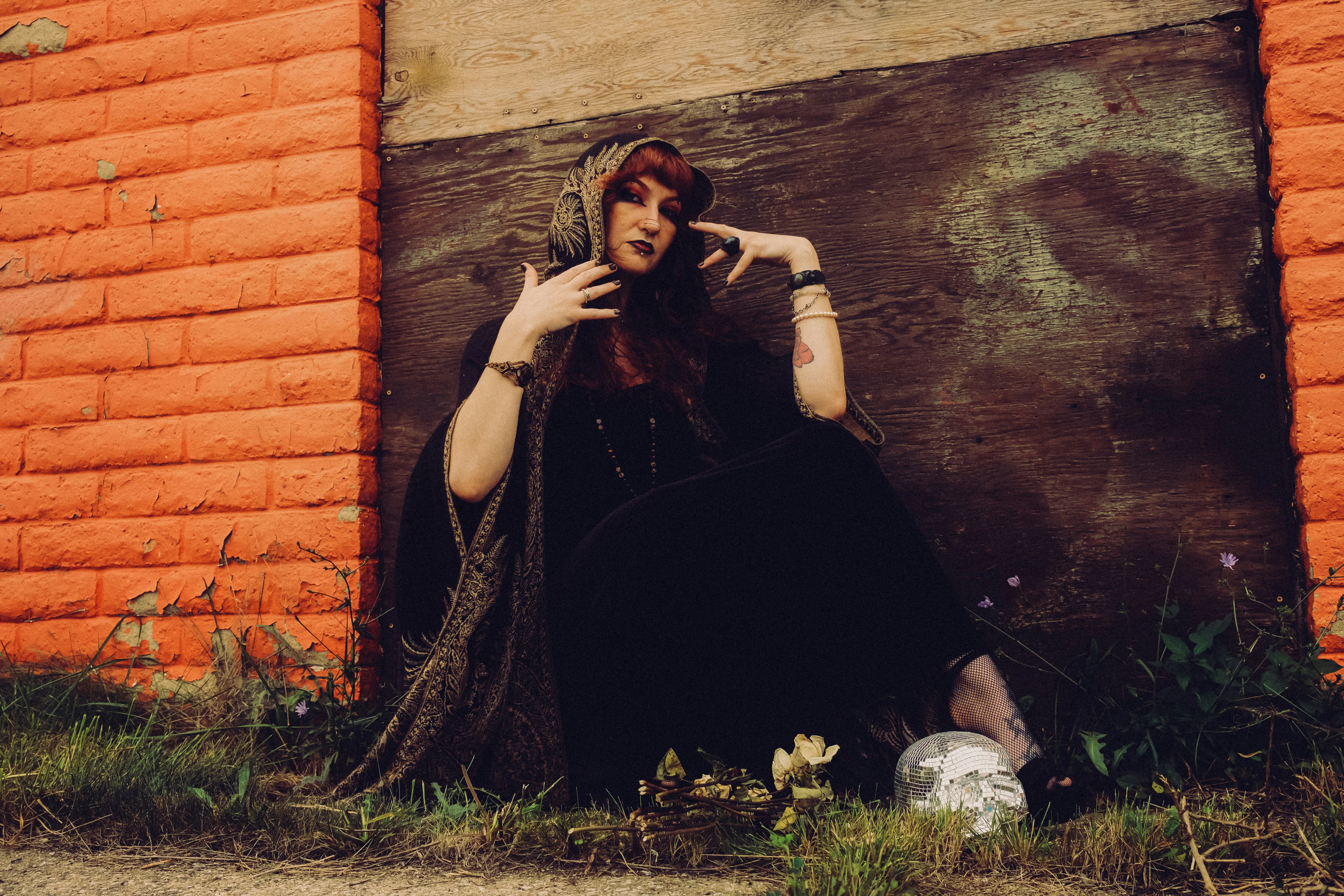 A person in a black hooded cloak sitting against an orange brick wall