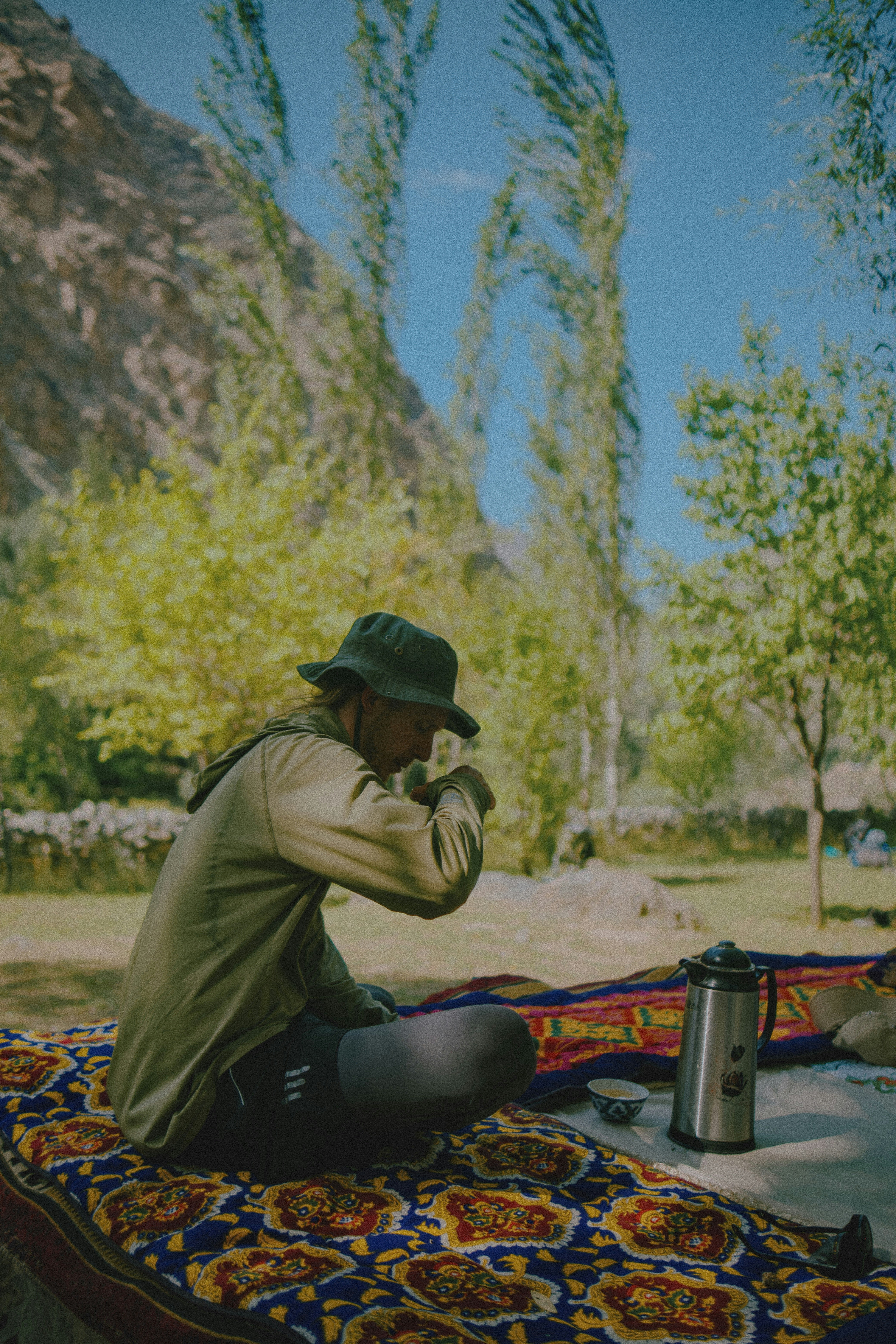 A person in a bucket hat drinking from a cup on a patterned rug
