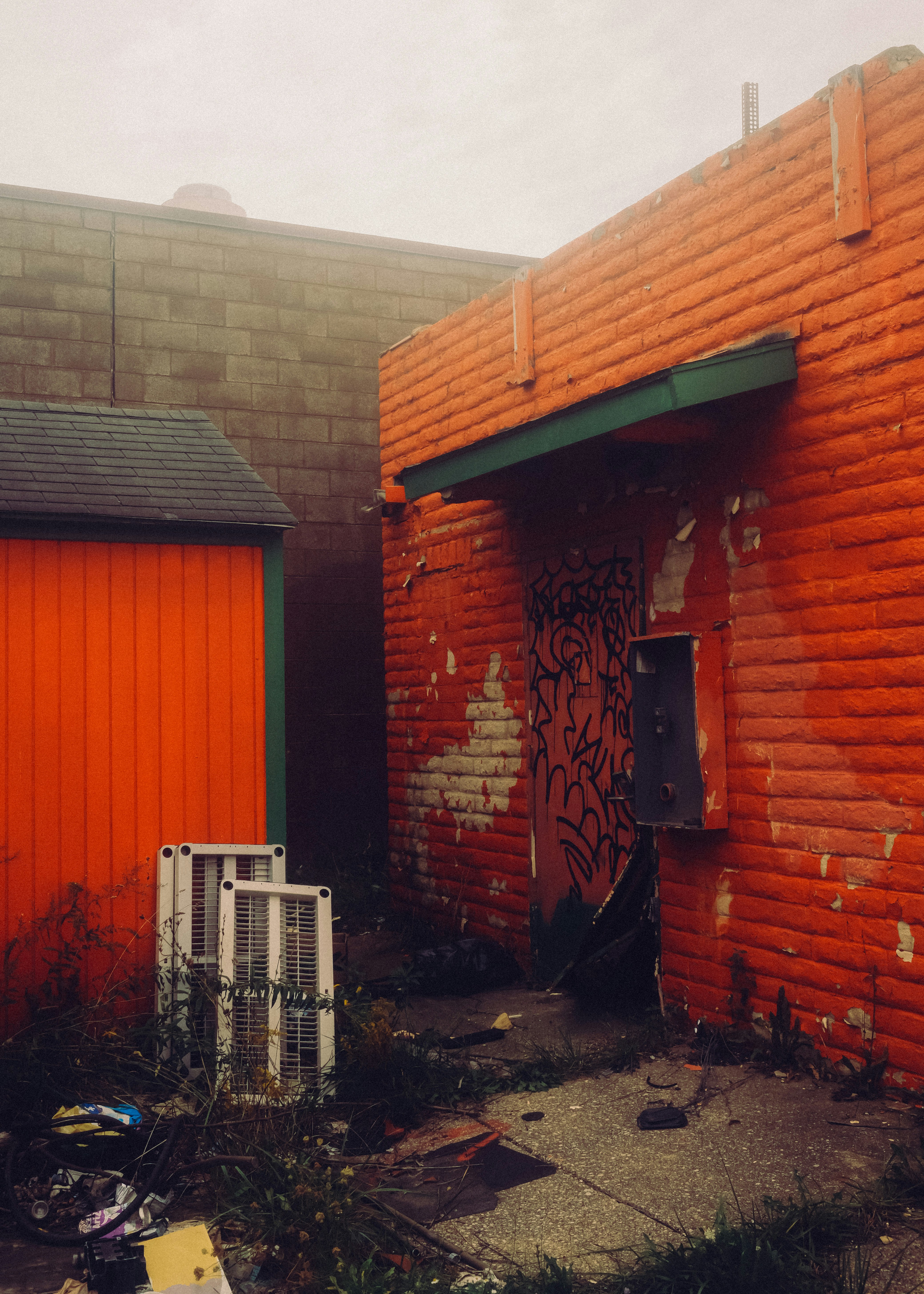 An orange brick building with graffiti on a door and discarded white vents