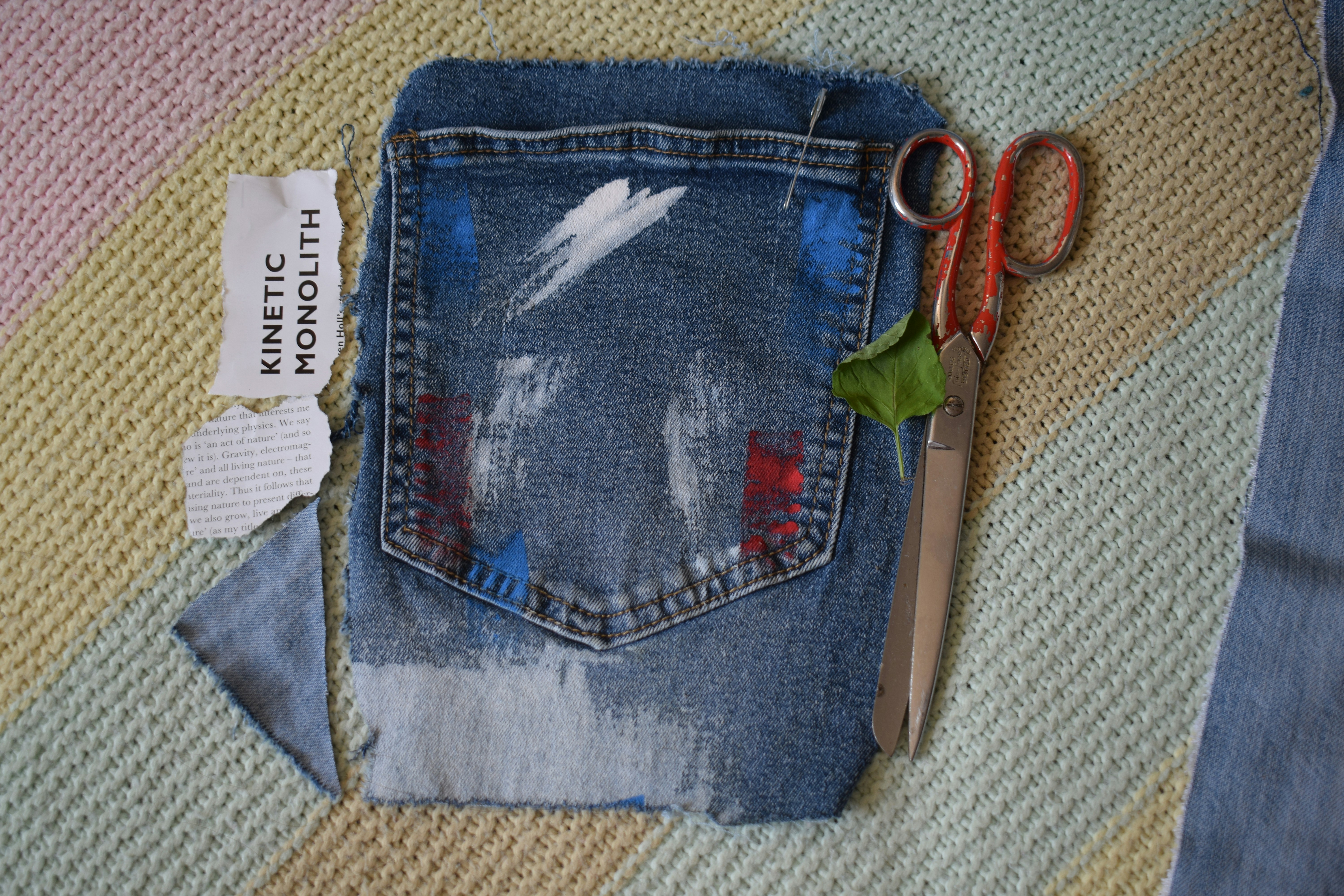 A denim pocket with paint marks, scissors, and paper on a textured surface