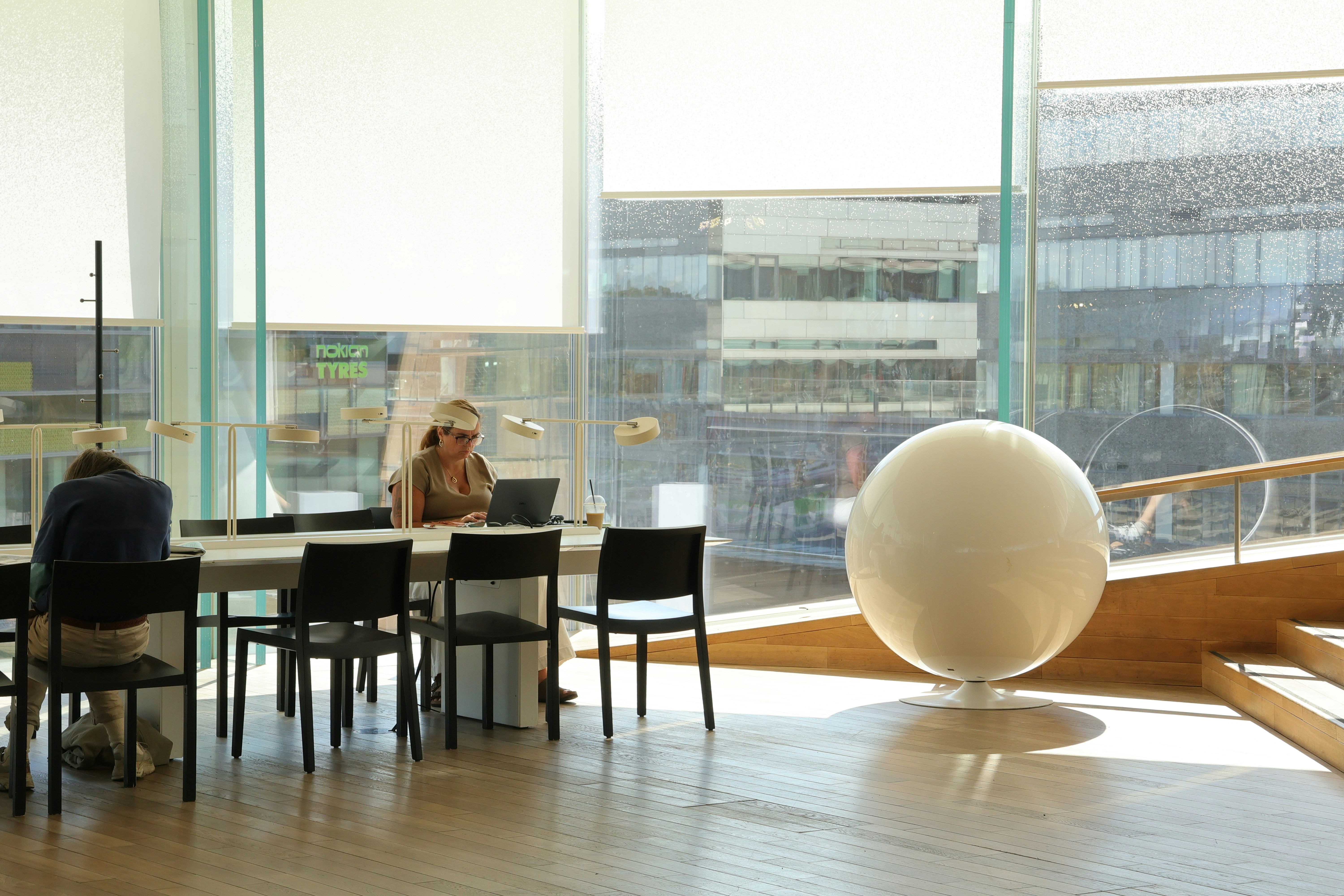 Two people working on laptops at a long table in a sunlit library