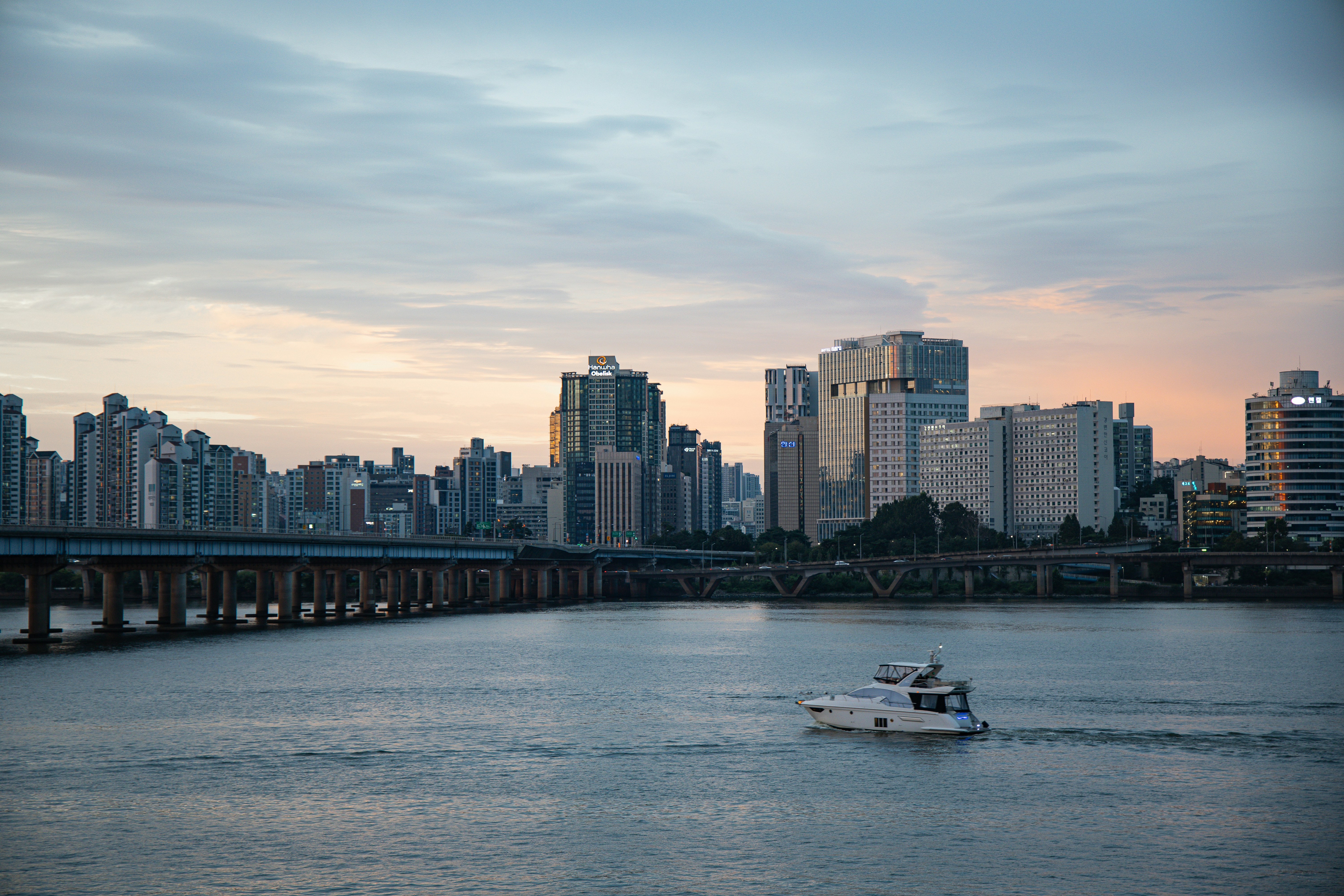 A white motorboat cruising on the Han River in Seoul with city skyscrapers