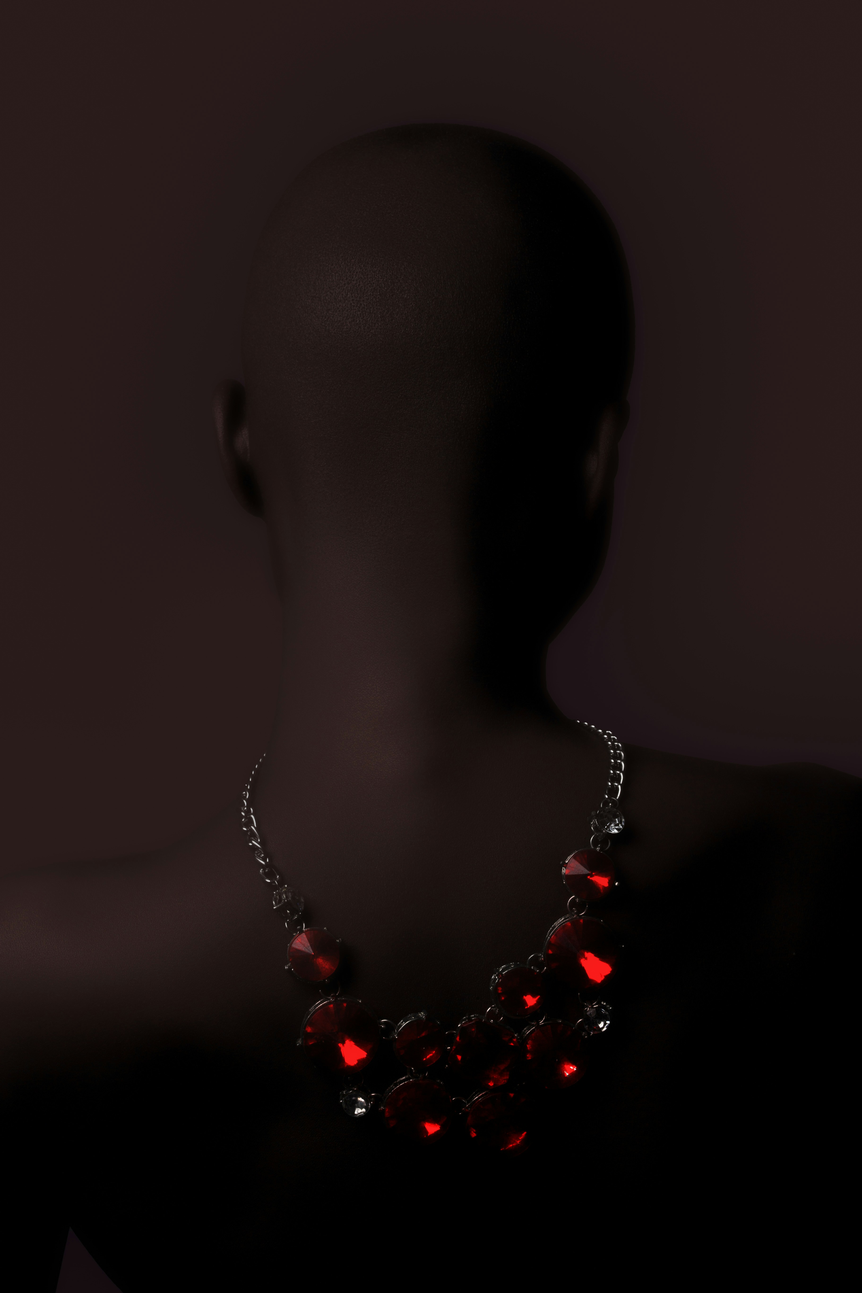 A dark mannequin wearing a silver necklace with large red faceted stones