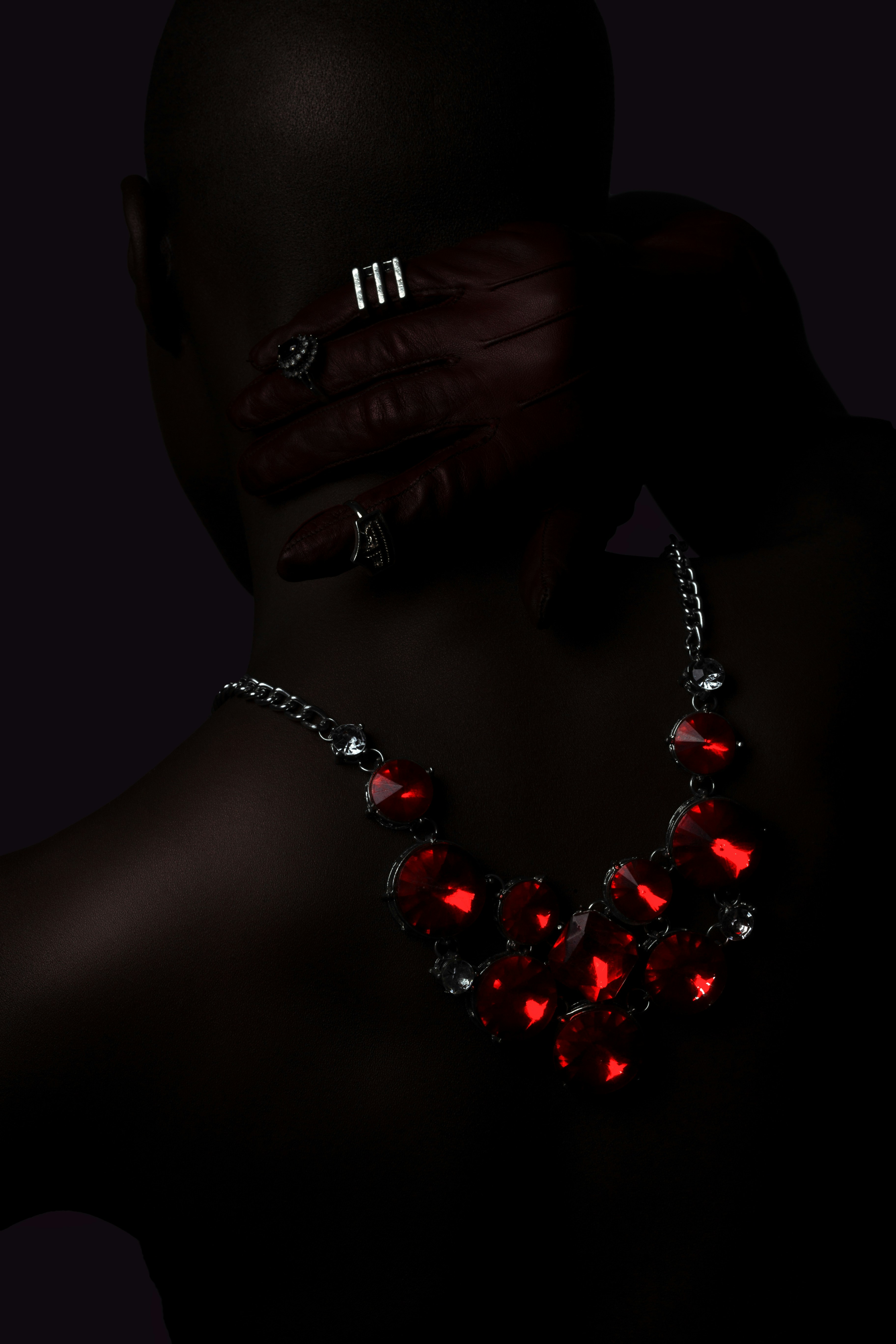 A person wearing a red crystal necklace and rings on a dark background
