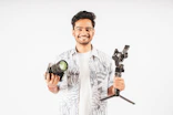 Smiling Indian content creator holding a camera and a gimbal in a bright studio