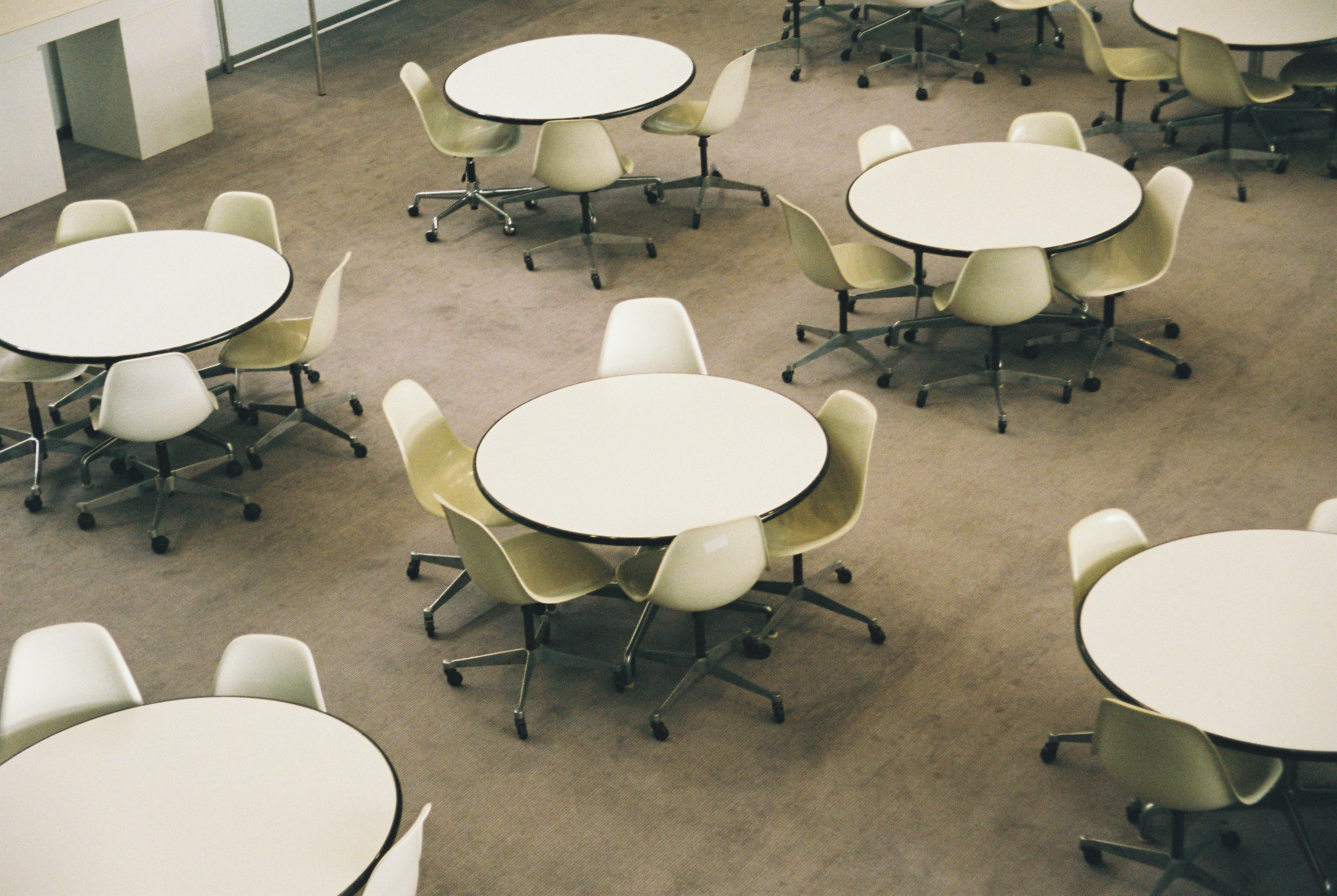 Cream swivel chairs around white round tables in a spacious common room