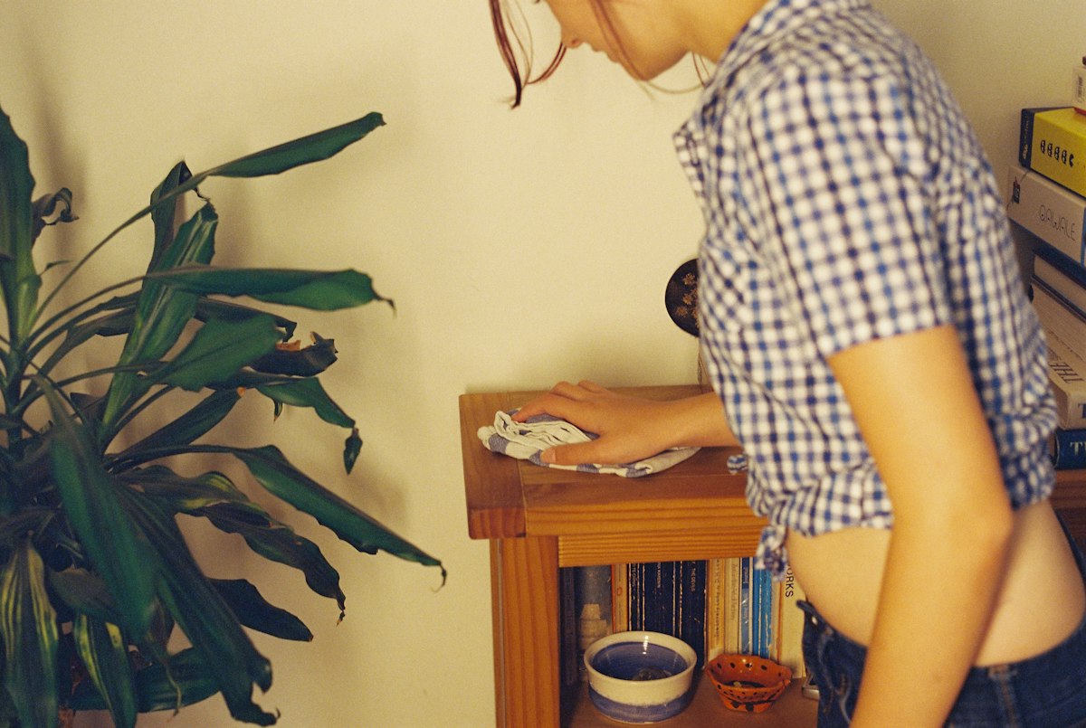 A woman wiping down a wooden cabinet with a cloth