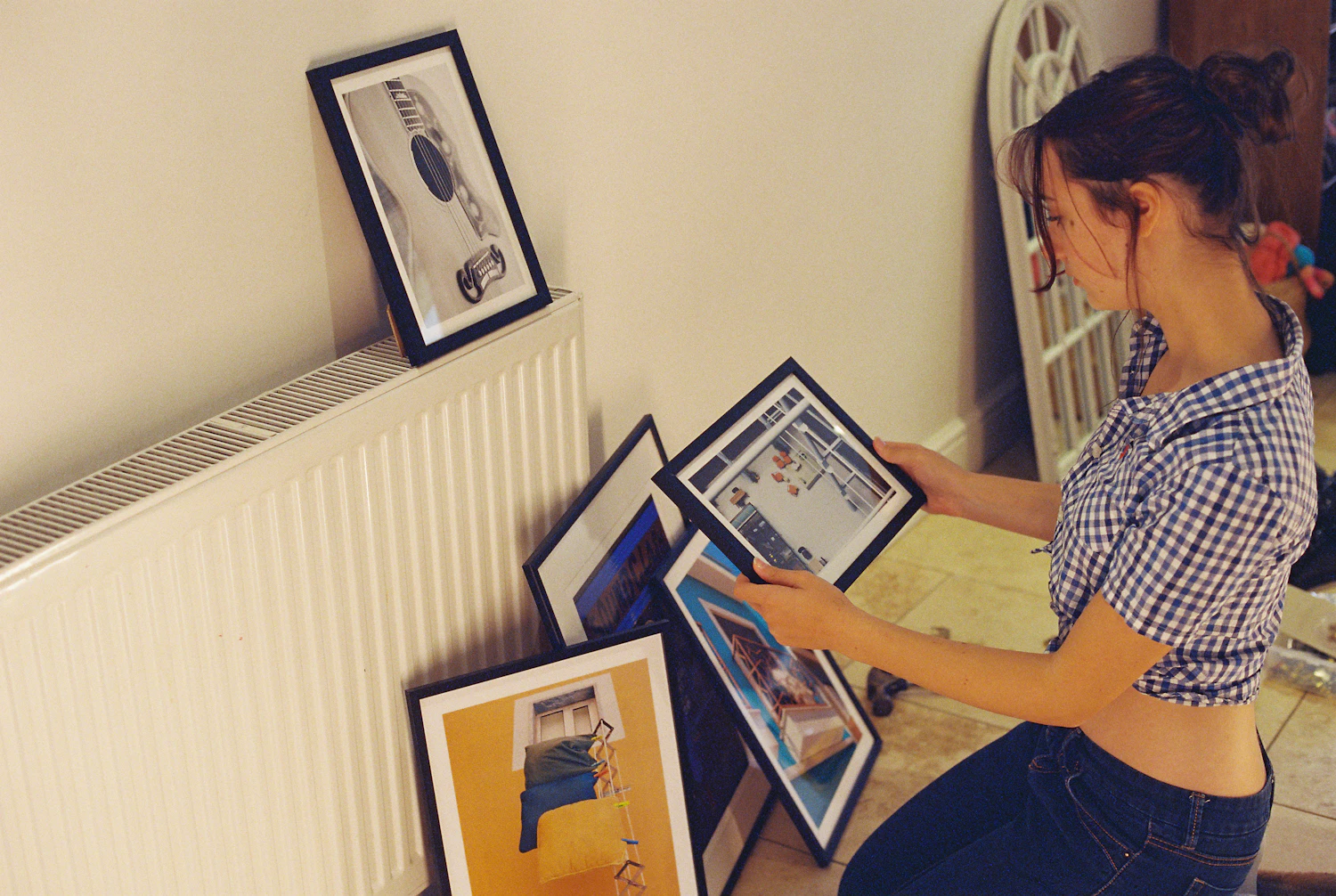 Framed works propped against a radiator in a flat, waiting to go up