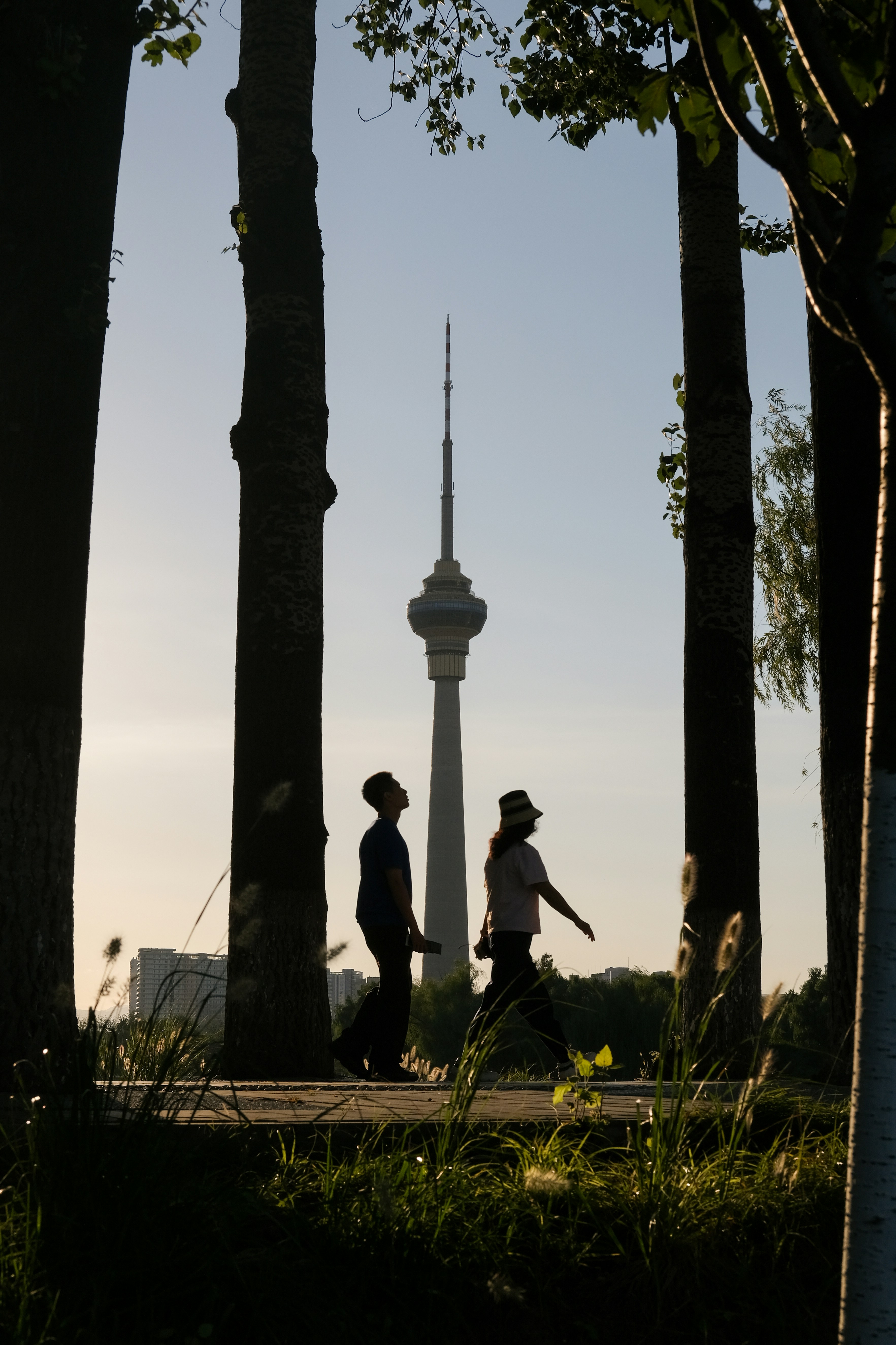 Deux personnes en silhouette marchant devant des arbres avec la tour centrale de la radio et de la télévision