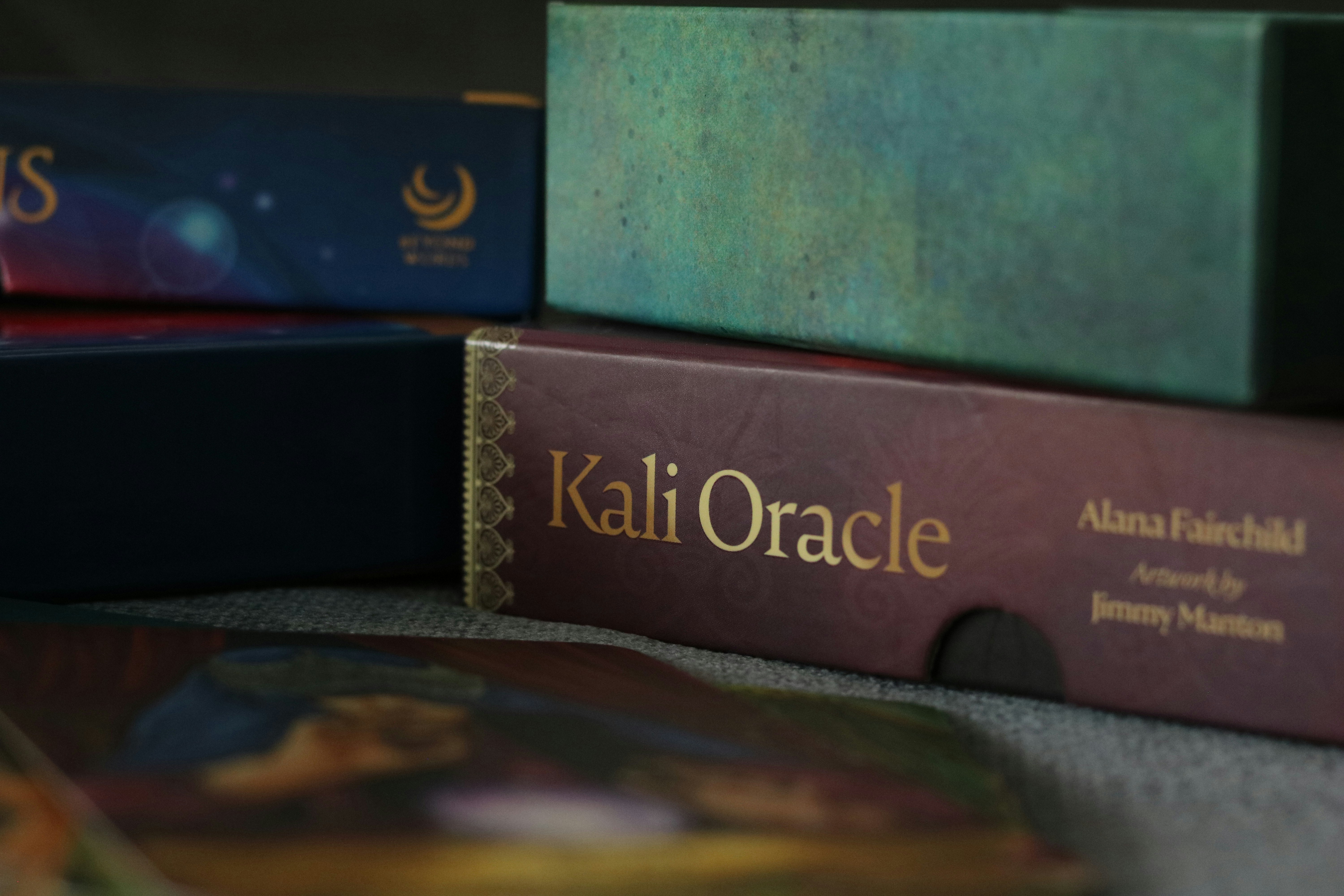 A stack of oracle card boxes including one labeled Kali Oracle on a grey surface