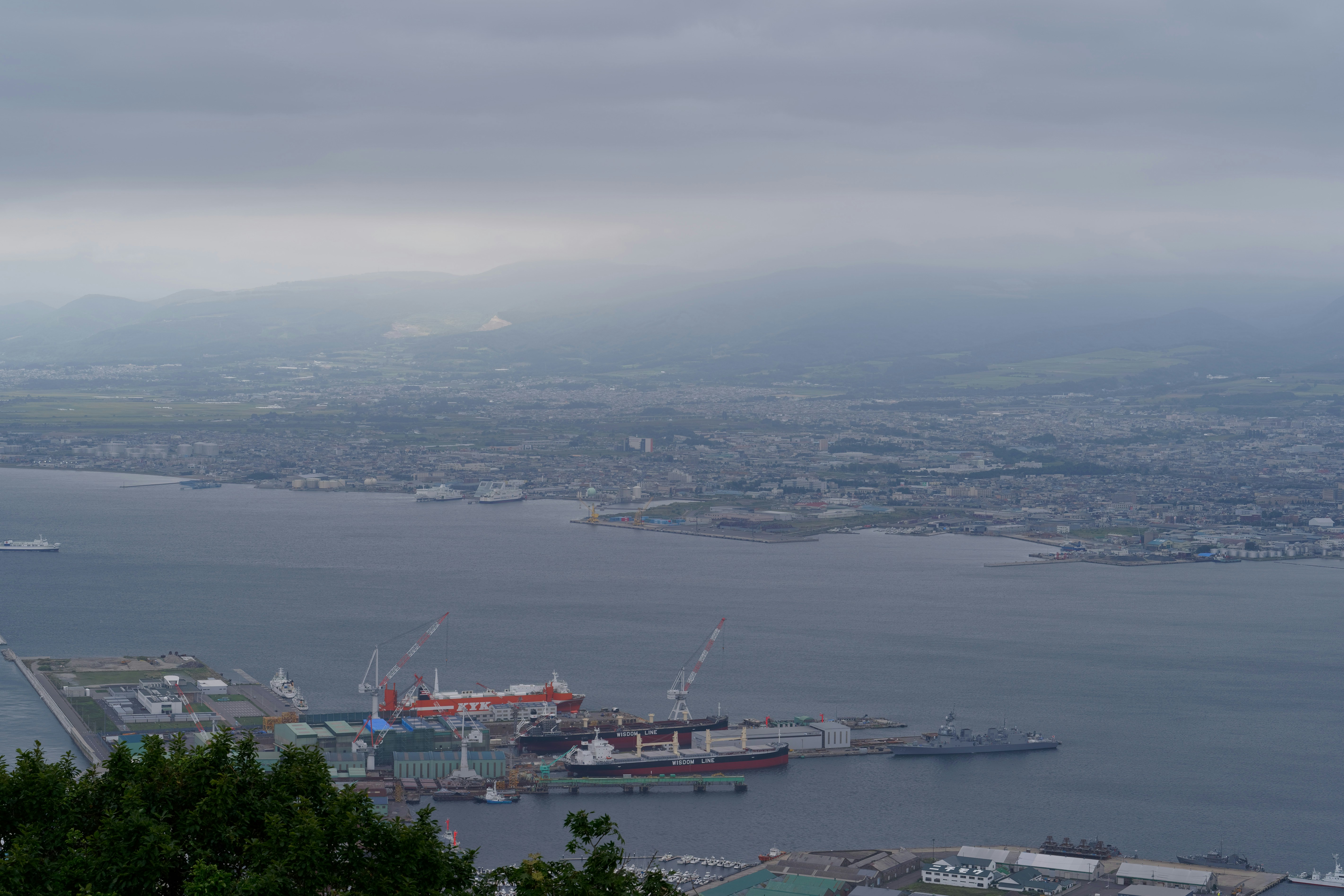 A coastal city and industrial harbor with cargo ships under a cloudy sky