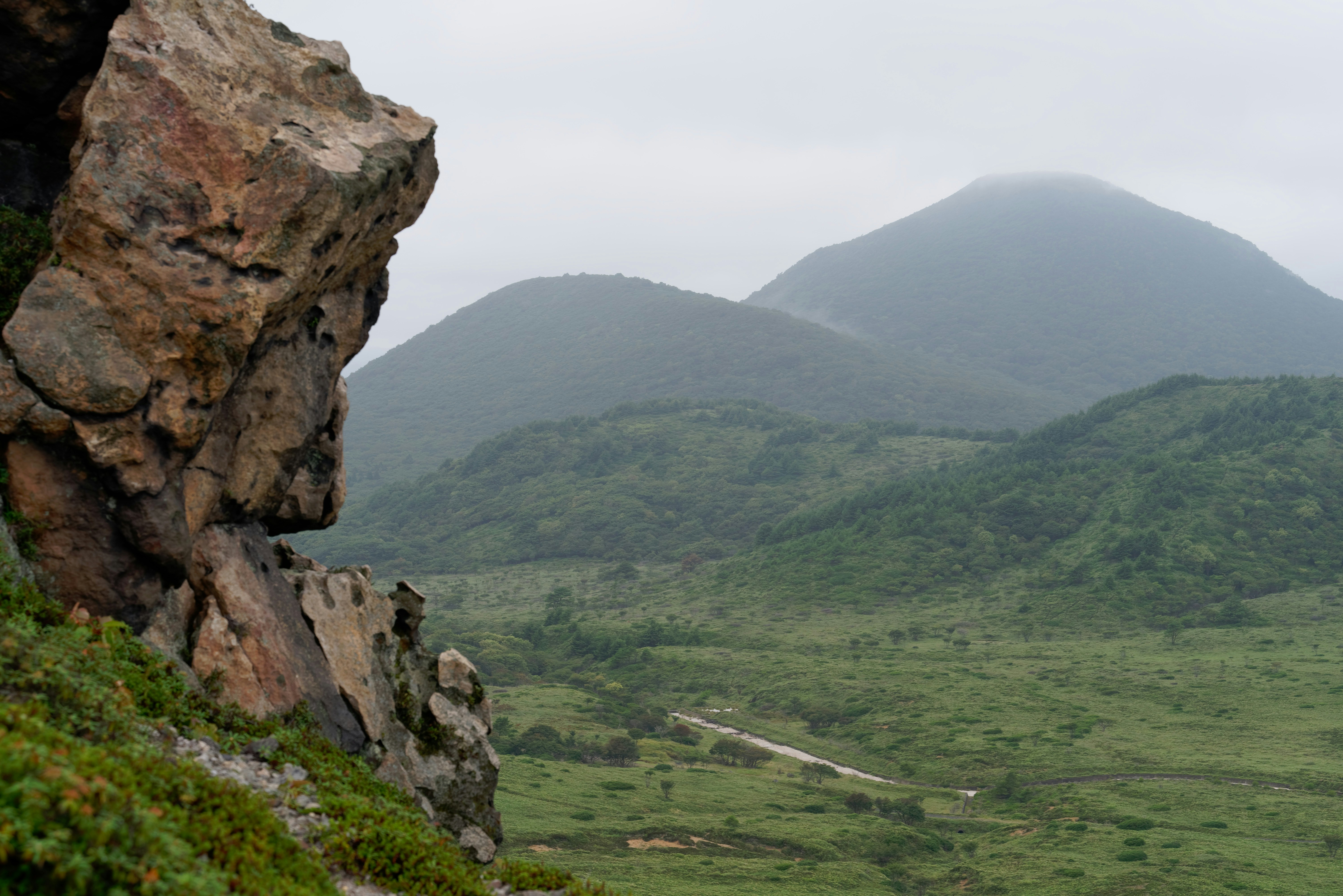A large jagged rock in the foreground overlooking a misty green mountain valley