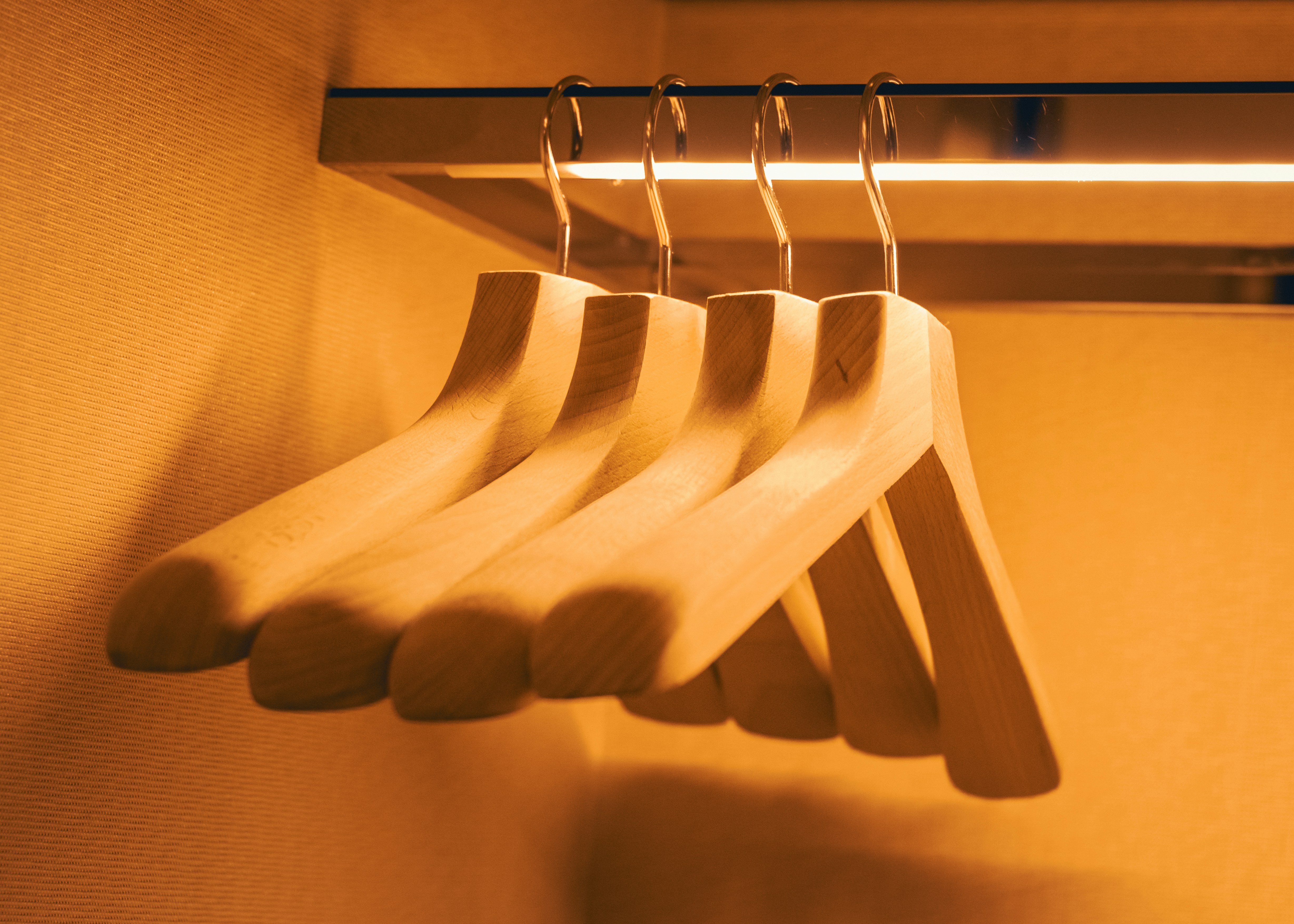 Four wooden clothes hangers hanging on a metal rod in warm light