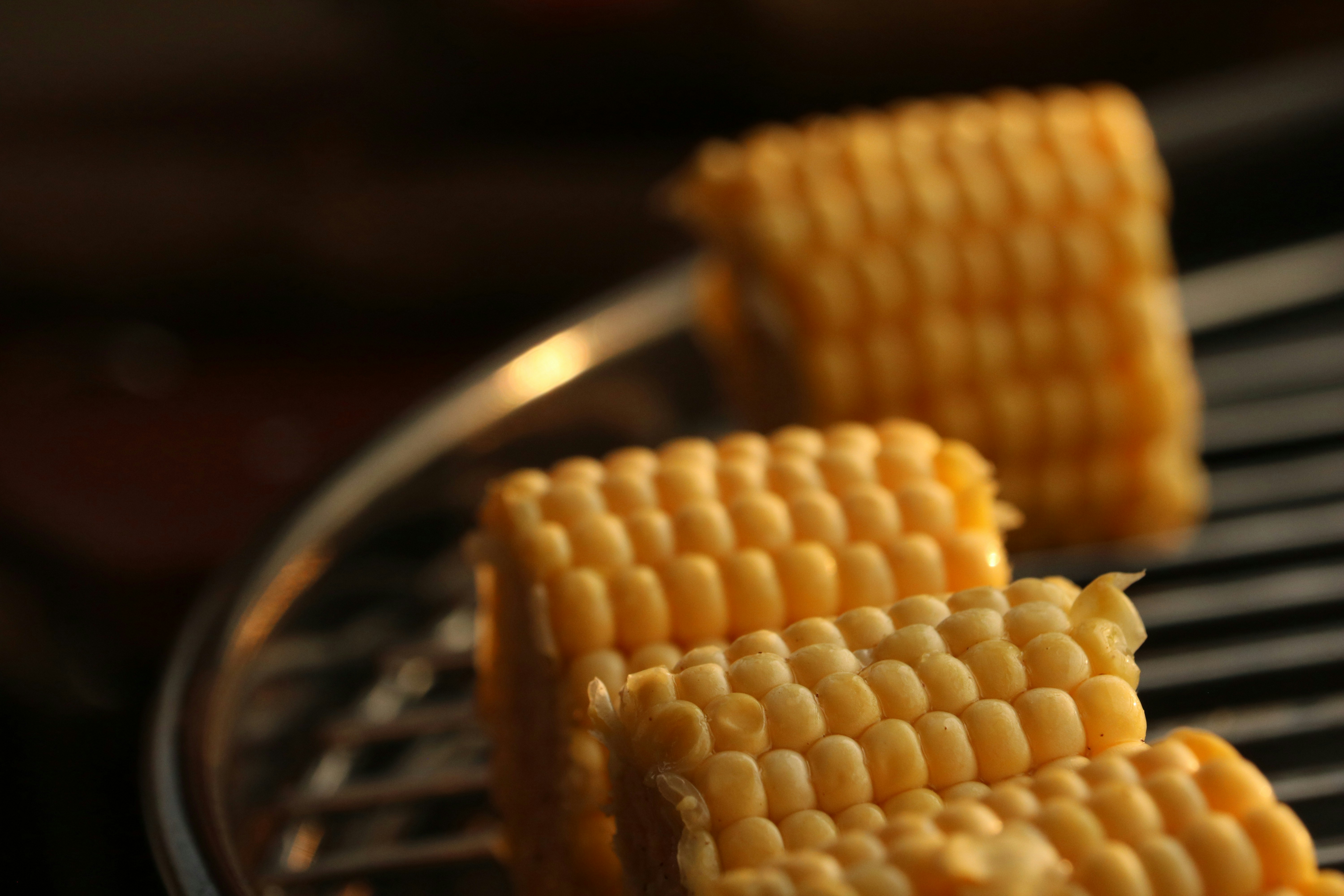 Three pieces of yellow corn on a metal grill grate in warm light