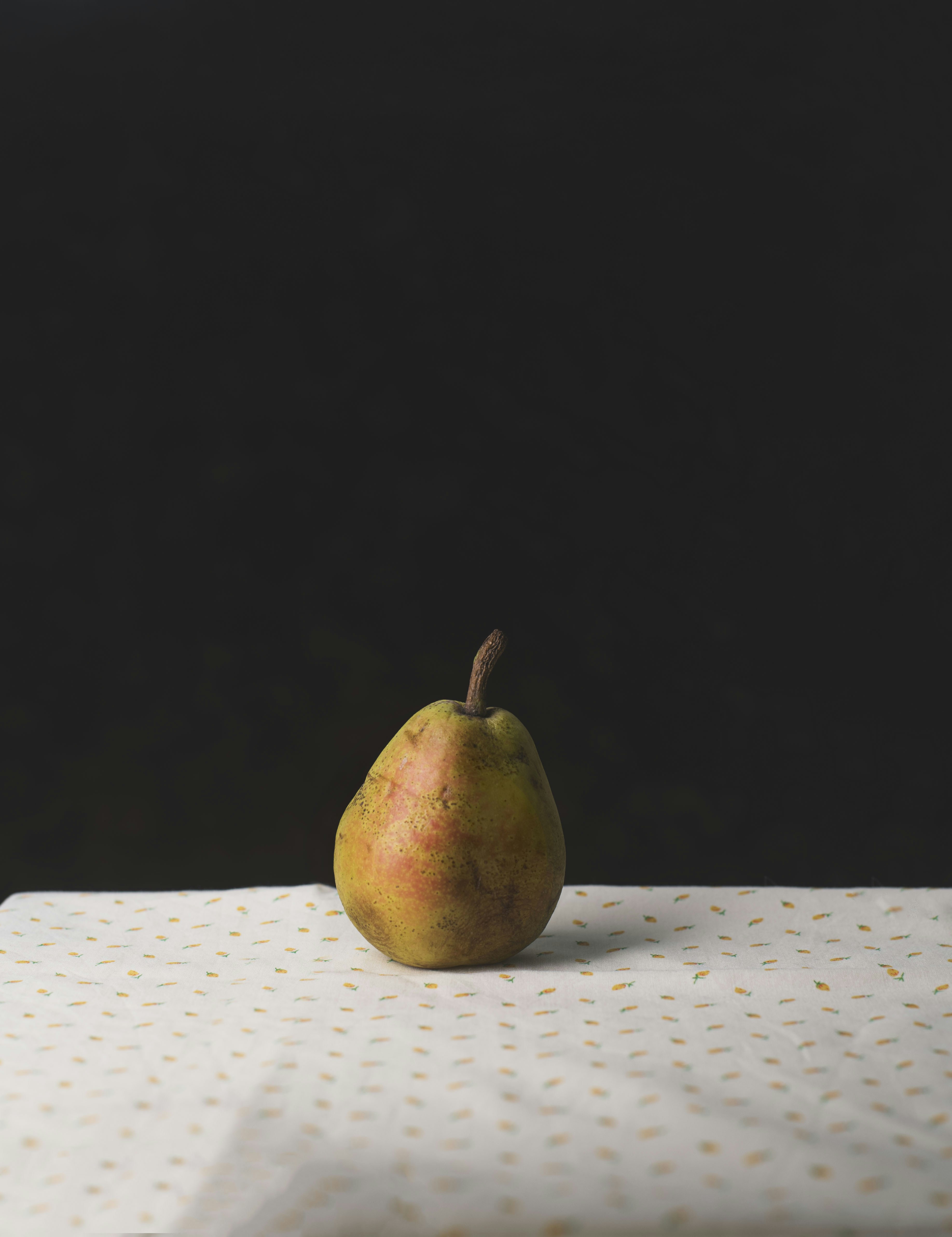A single ripe pear on a white cloth with a small yellow pattern