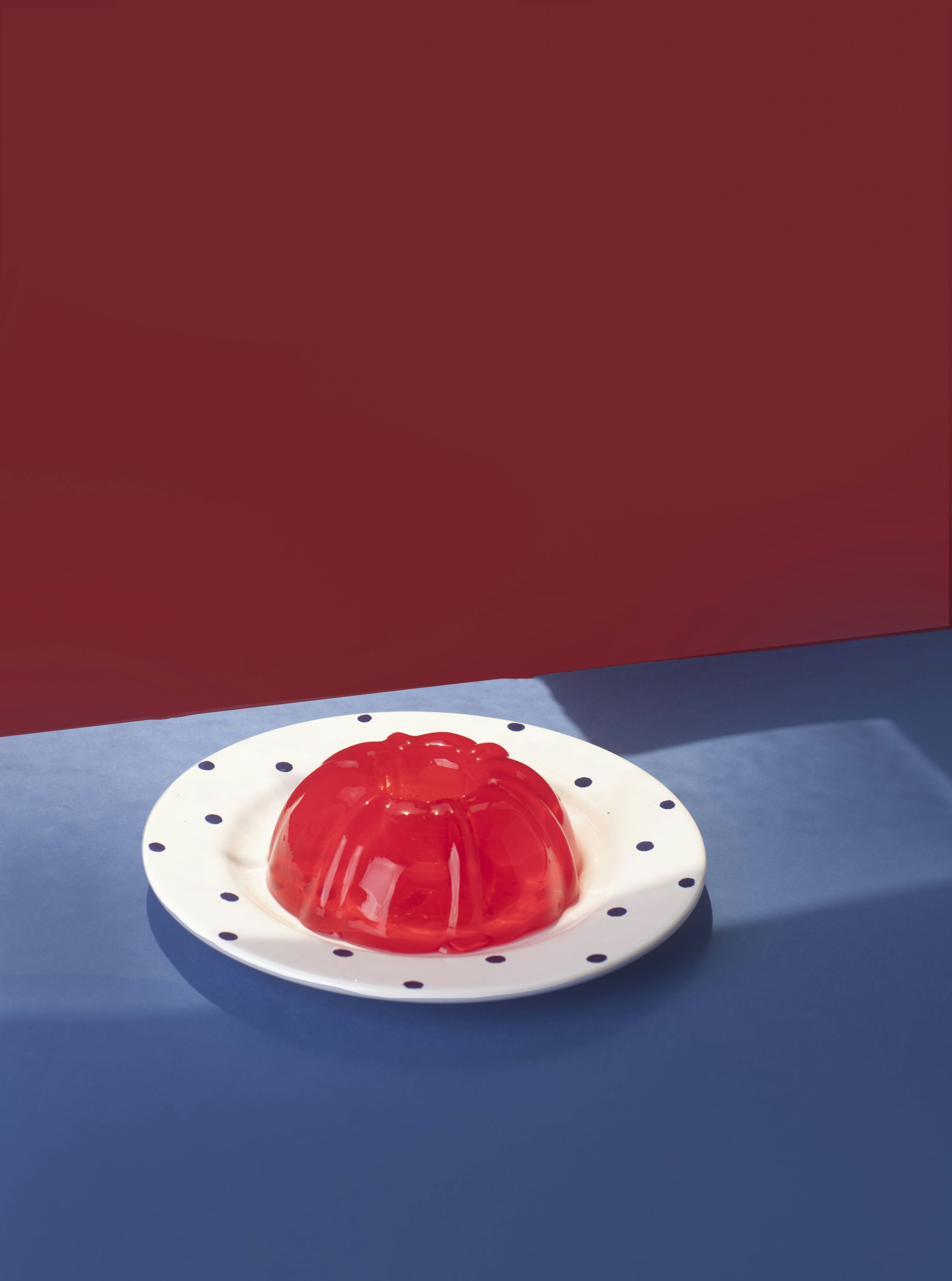 A red gelatin mold on a white plate with blue dots