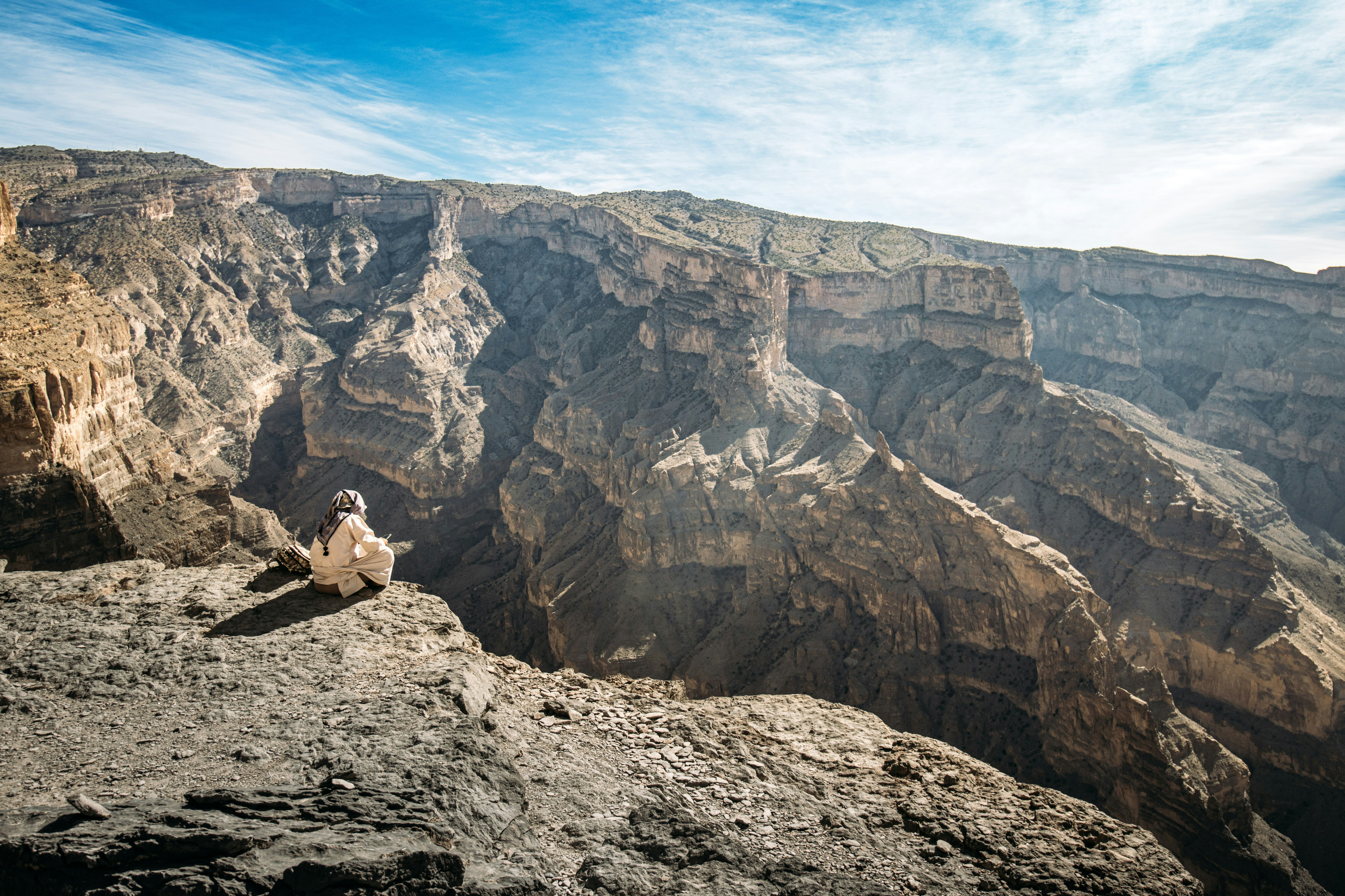 Escursionista in abiti tradizionali sul bordo del canyon del Wadi Ghul, Jebel Shams, Oman
