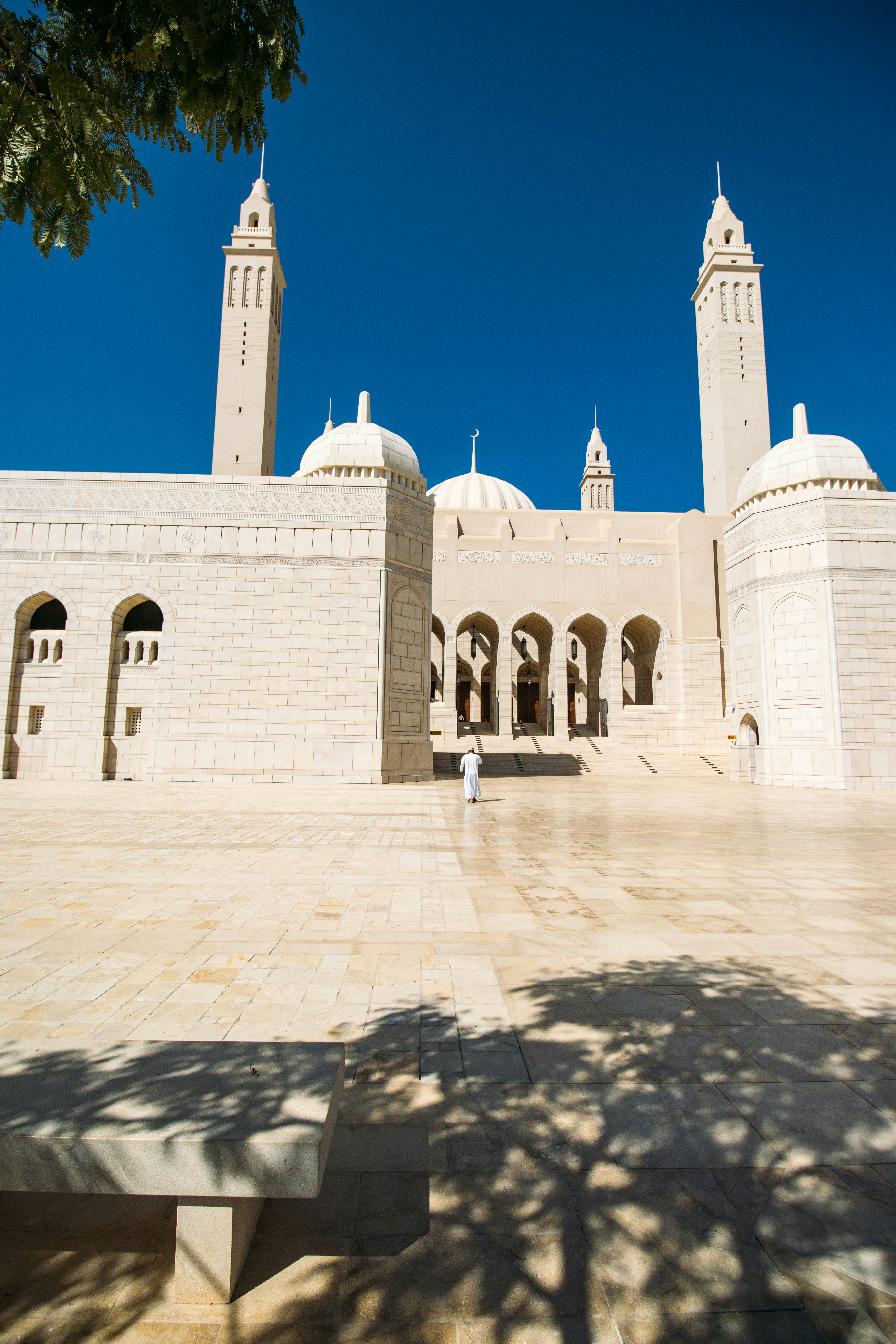 Uma pessoa em um thobe branco caminhando em direção a uma grande mesquita com altos minaretes