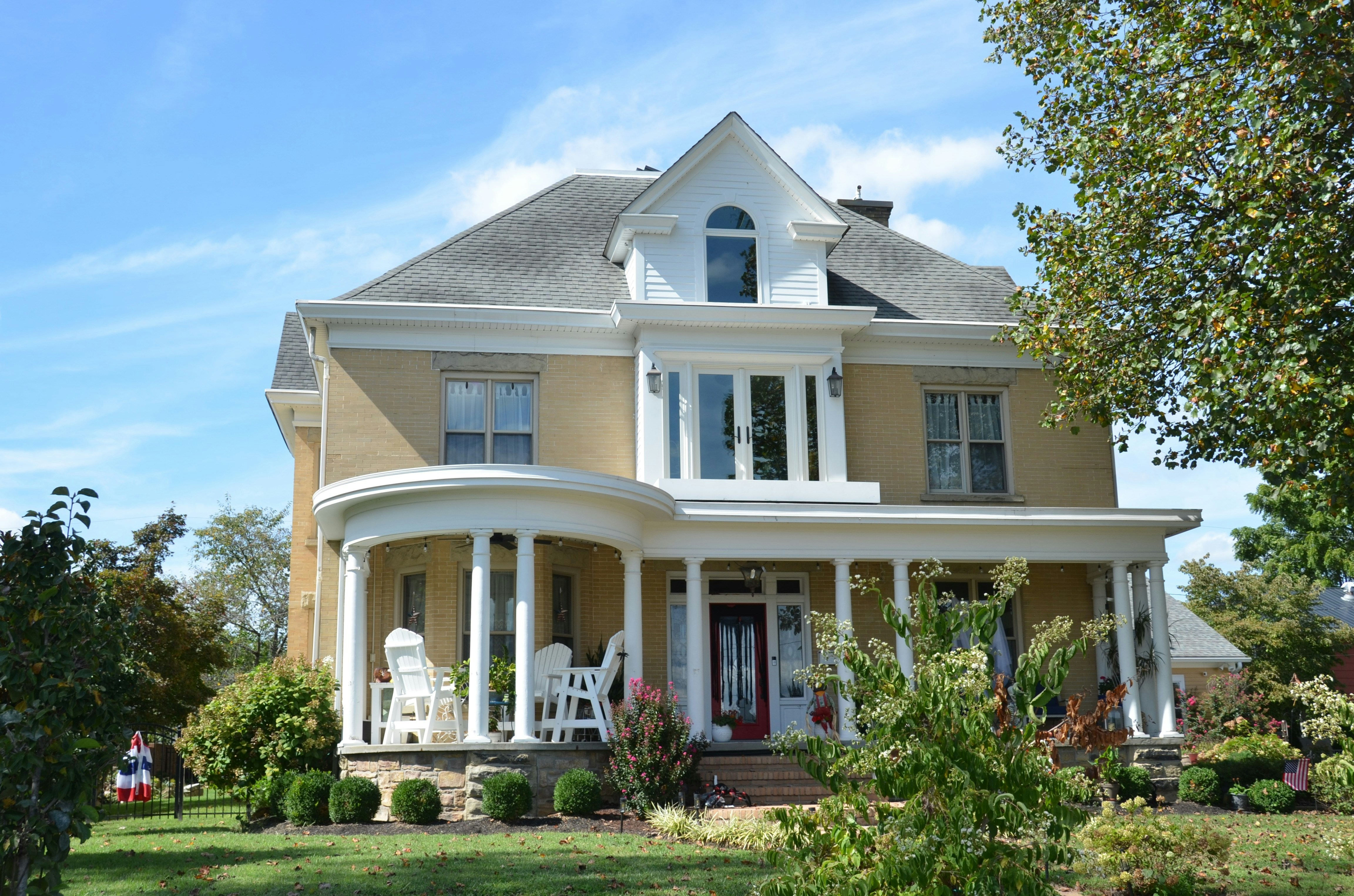 A yellow brick house with a white porch and columns under a blue sky