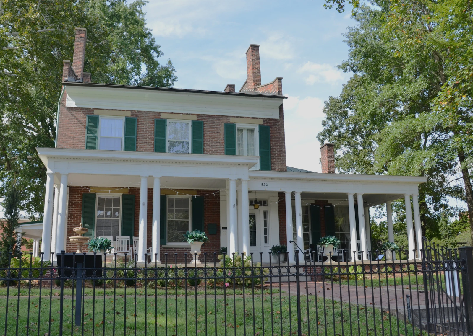 A classic Southern brick home with green shutters and a white columned porch