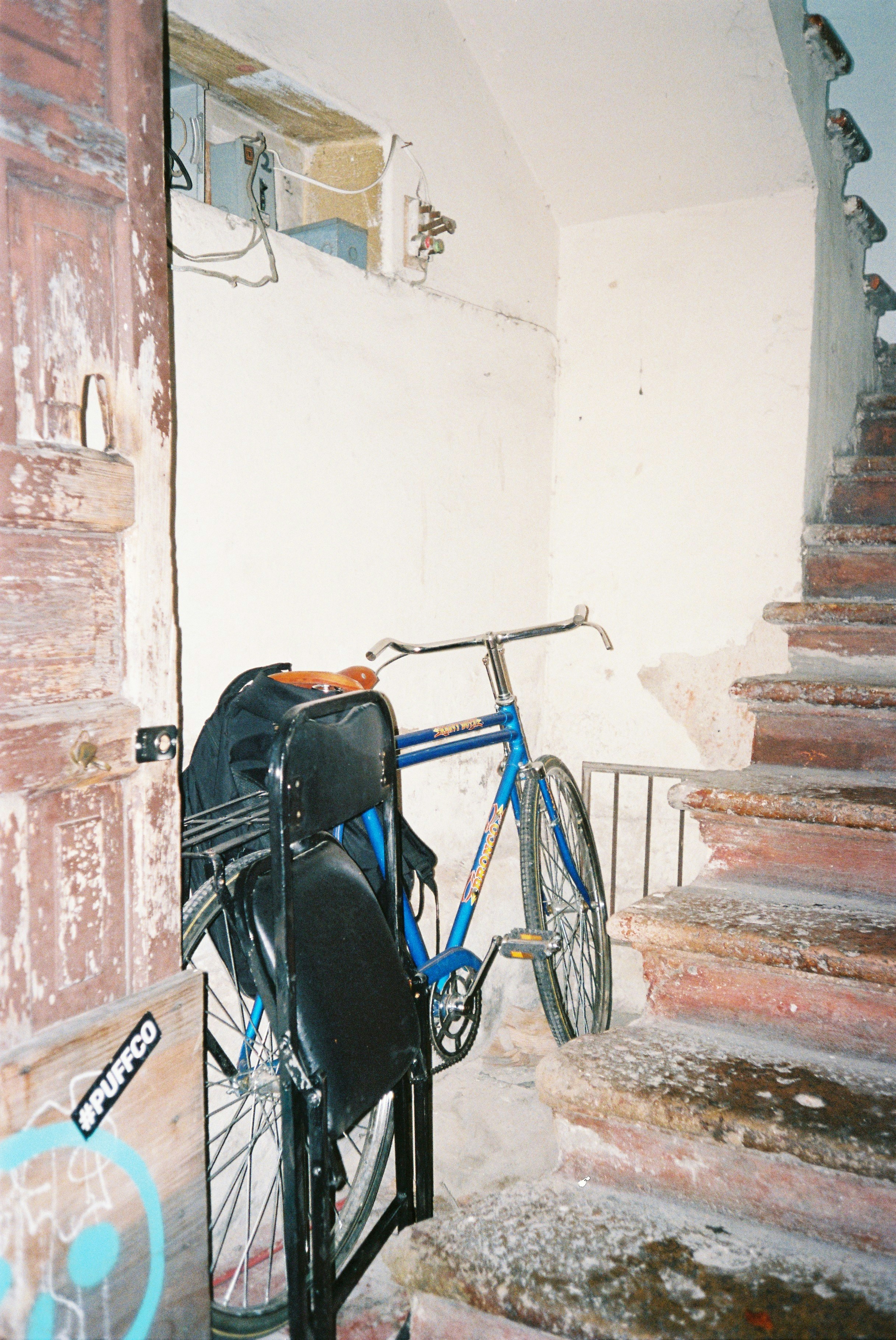 A blue bicycle parked beside a black folding chair near a wooden door