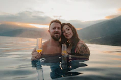 A man and a woman holding glasses in an infinity pool at Hotel Hubertus