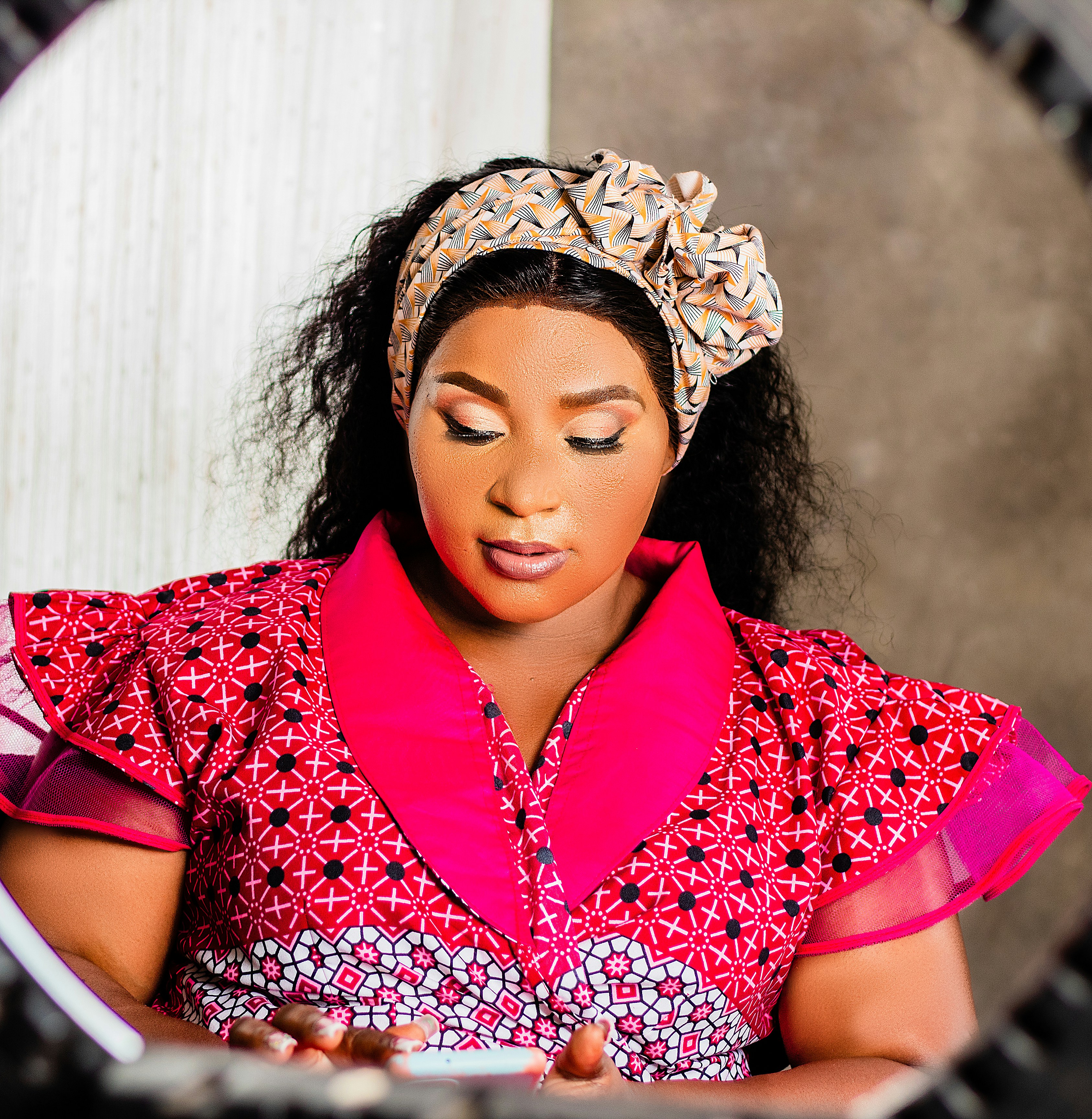 A woman in a patterned pink dress and headwrap looking at a smartphone