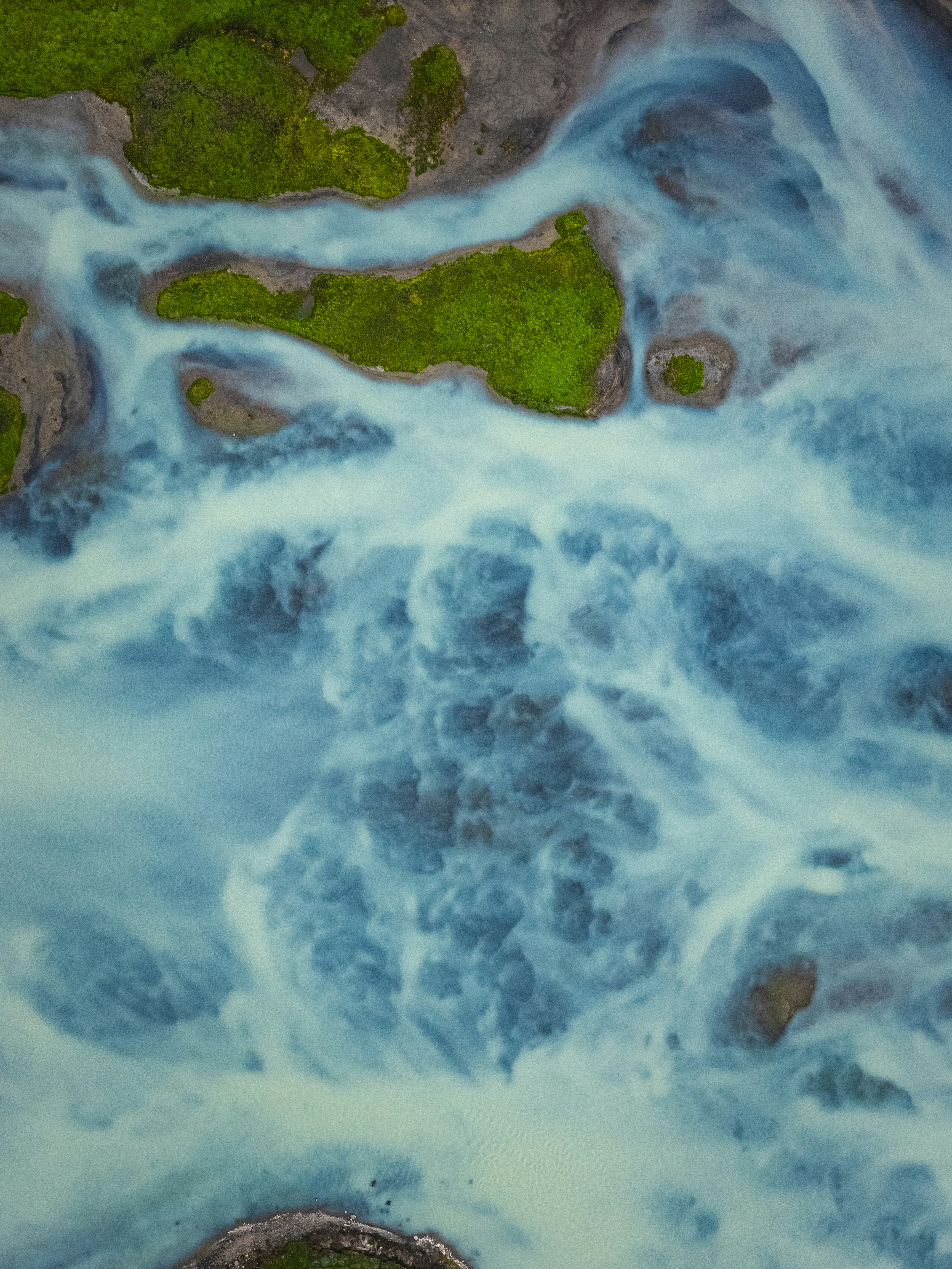An aerial view of a glacial river with bright green islands