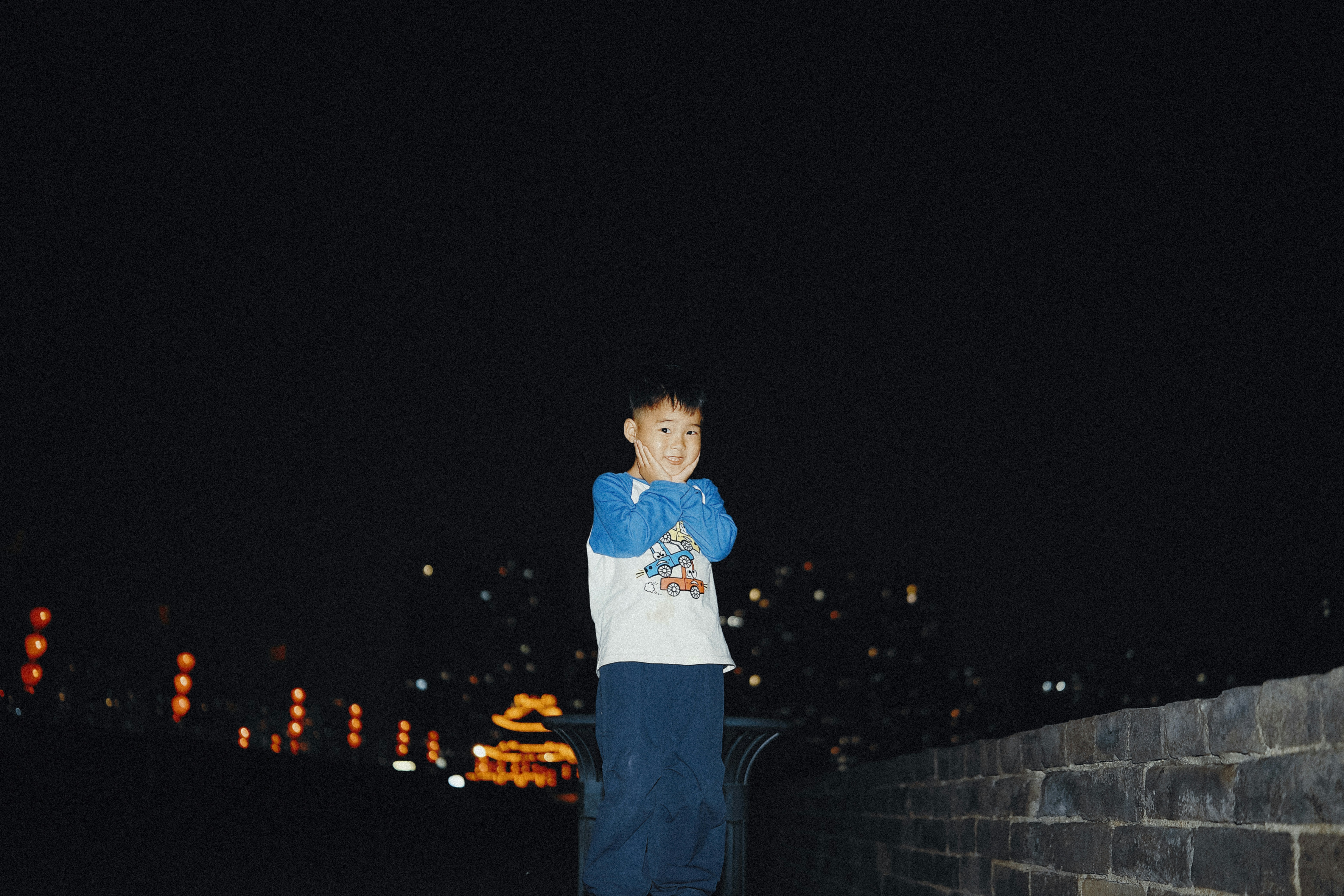 A child with hands on cheeks against a dark night background with city lights
