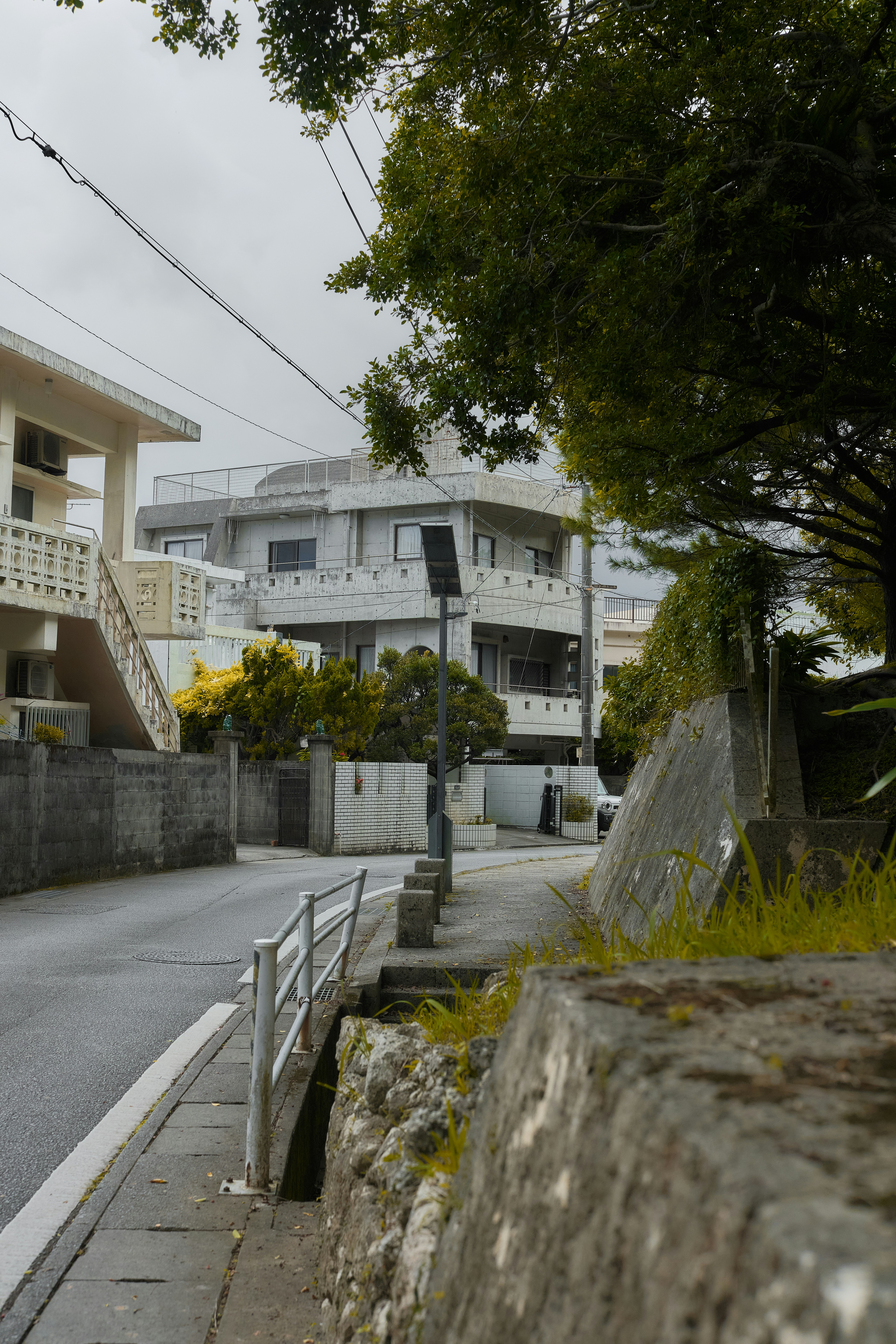 A quiet street with concrete buildings and a stone wall in Naha, Okinawa