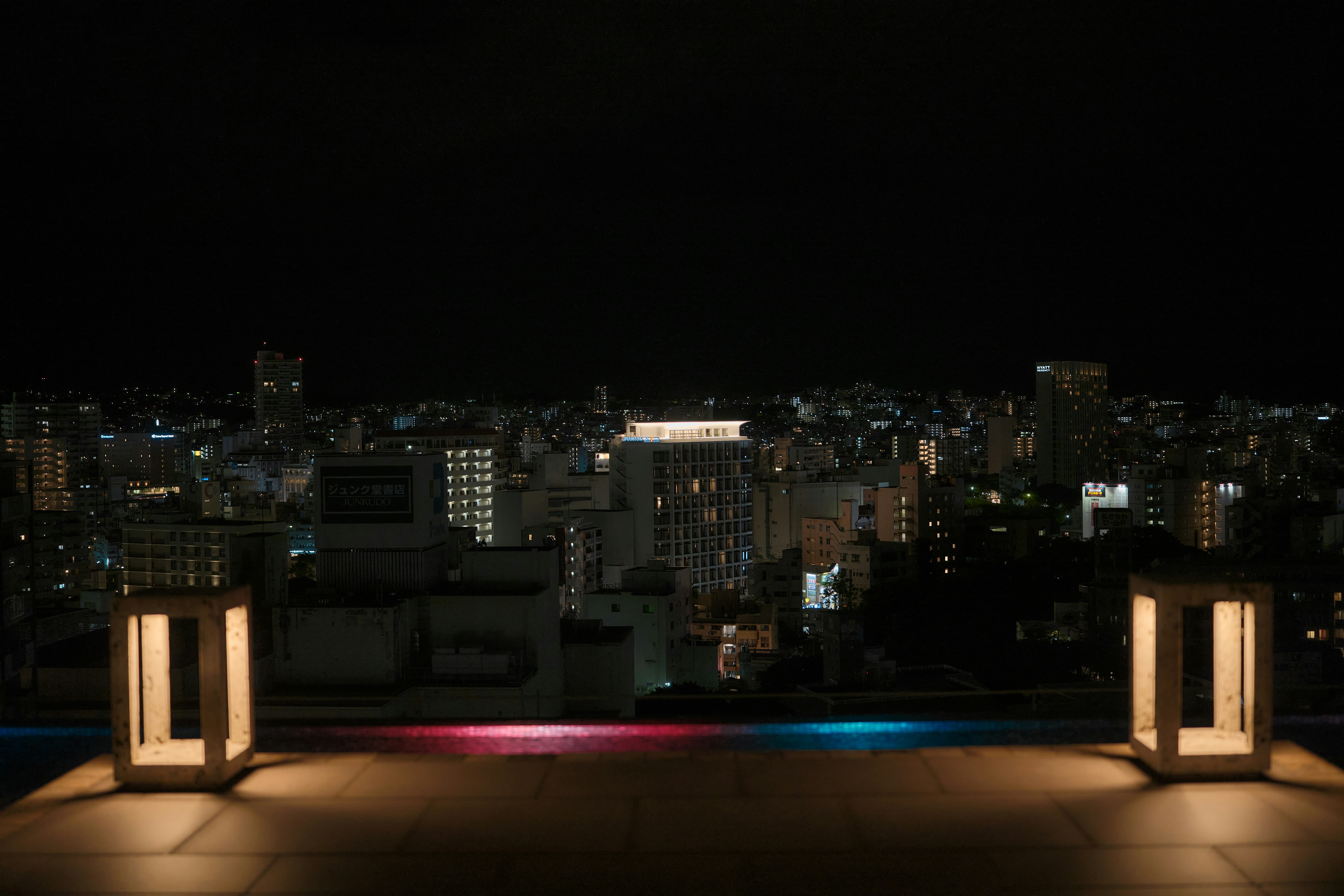 Two glowing lanterns on a terrace overlooking a city skyline at night