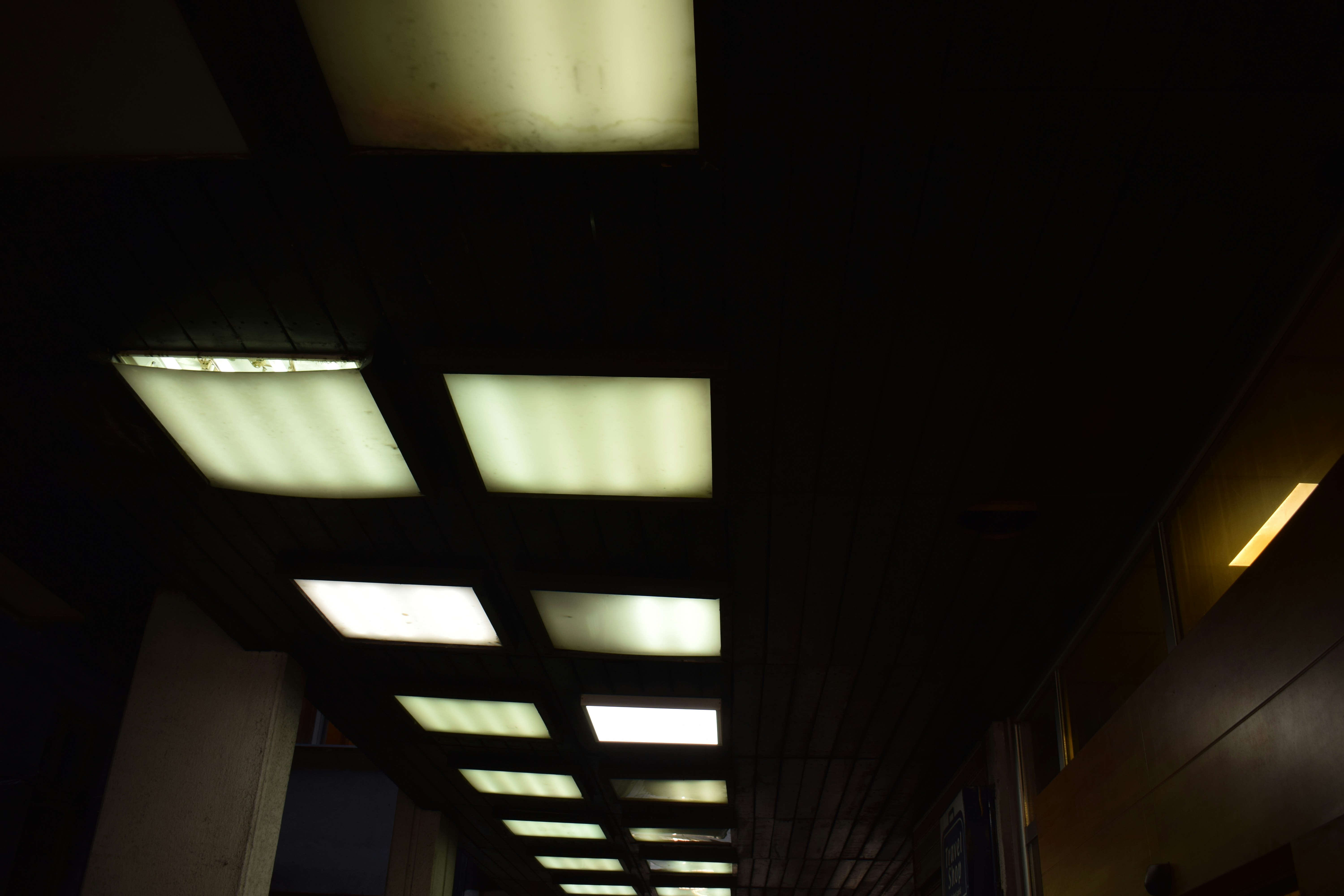 A row of recessed square ceiling lights in a dark wooden corridor