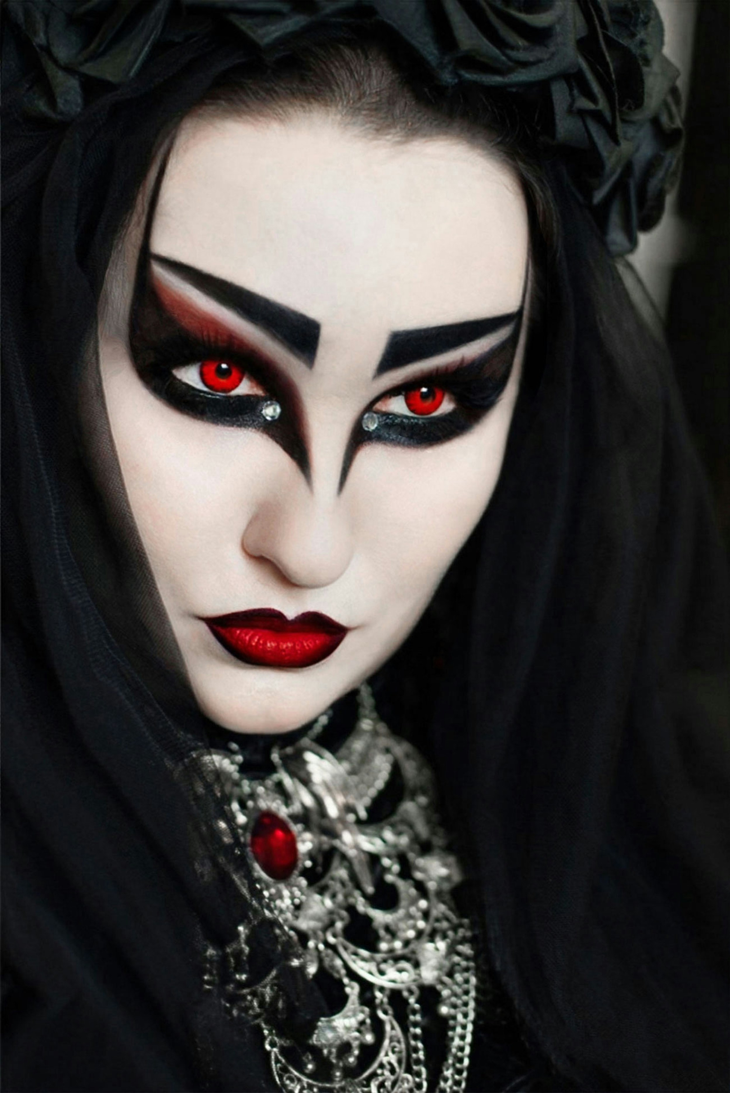 A person with red contact lenses and dramatic black makeup wearing a black veil