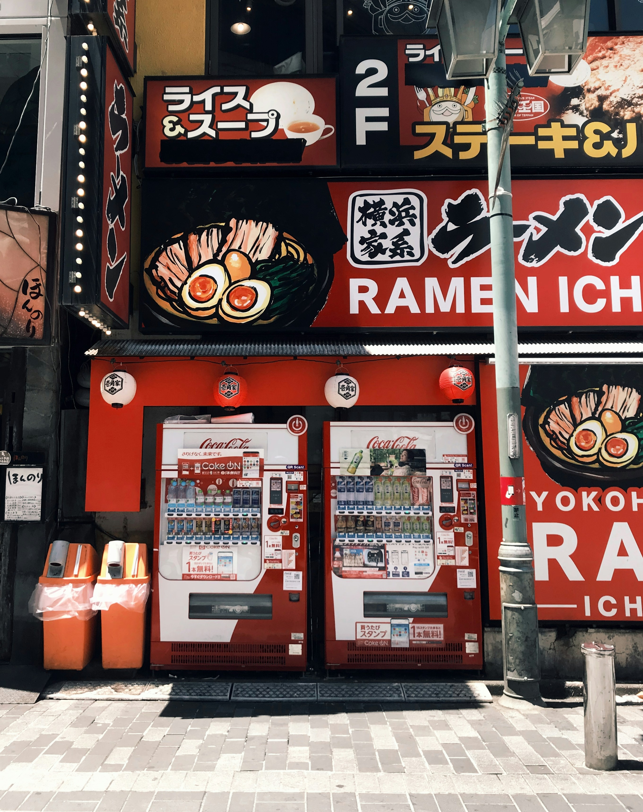 Two red vending machines in front of a ramen restaurant with bright signage