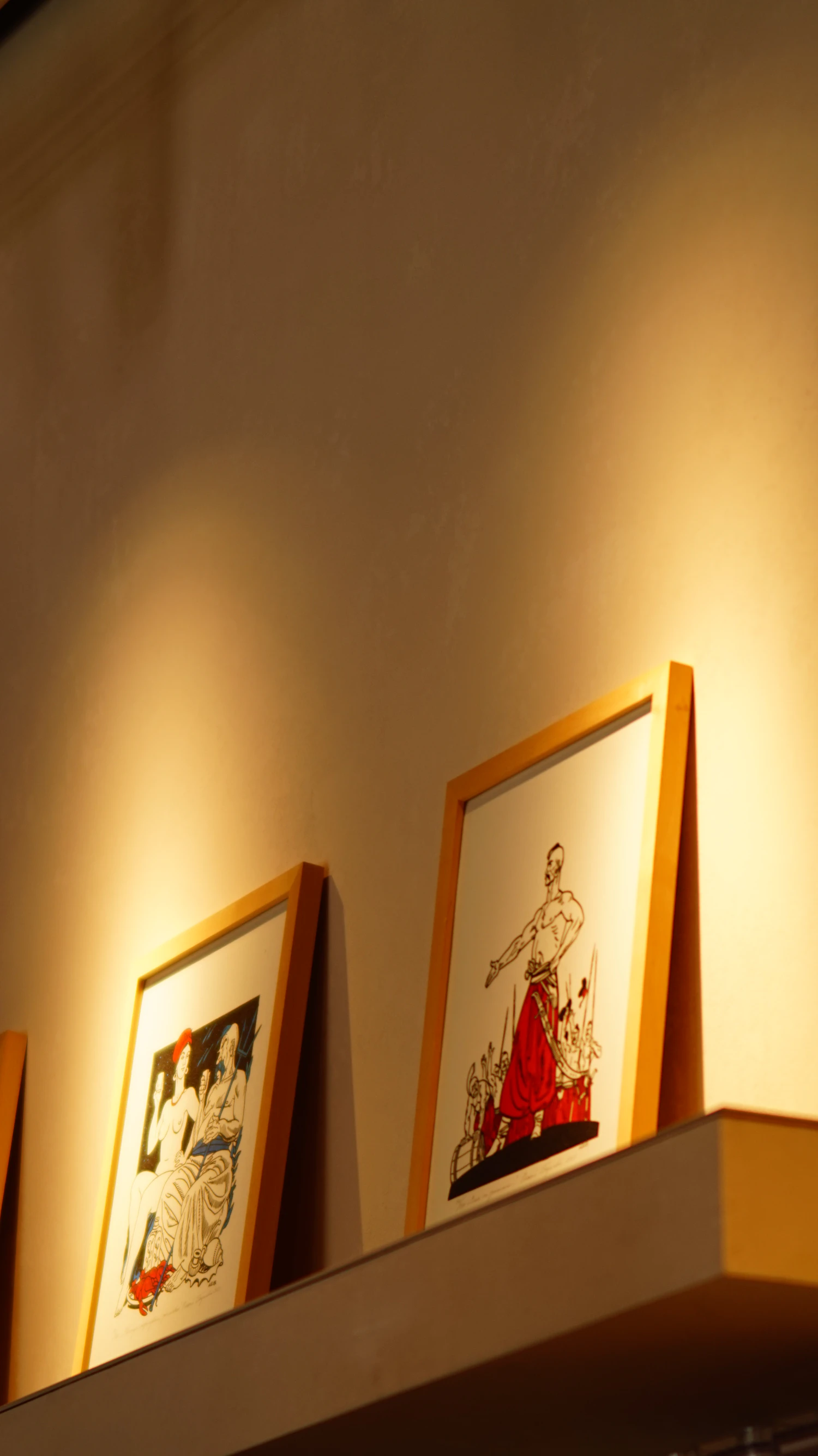 Two framed illustrations standing on a shelf against a warm beige wall